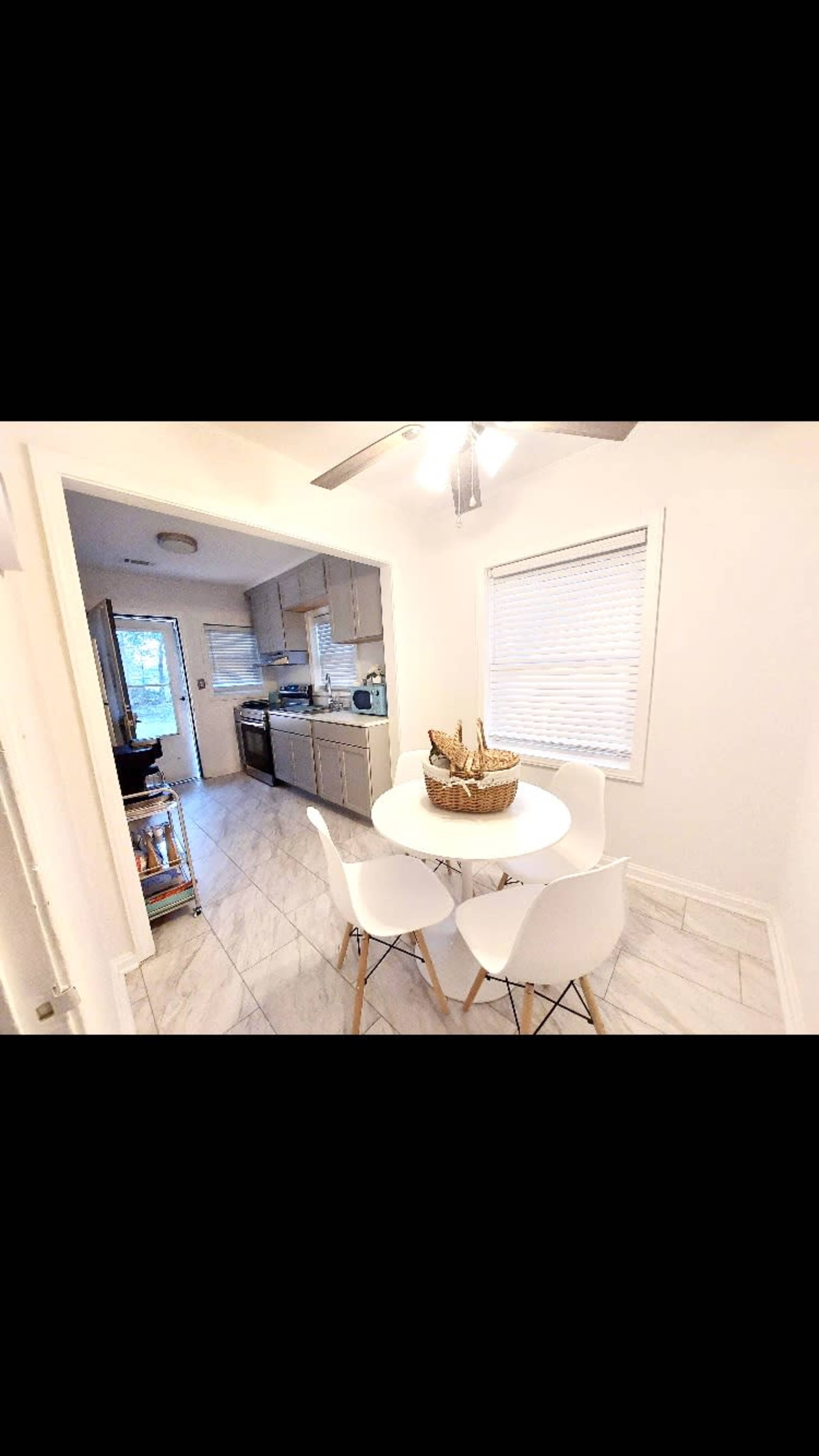 A small dining area features a round white table surrounded by four chairs, with a kitchen visible in the background.