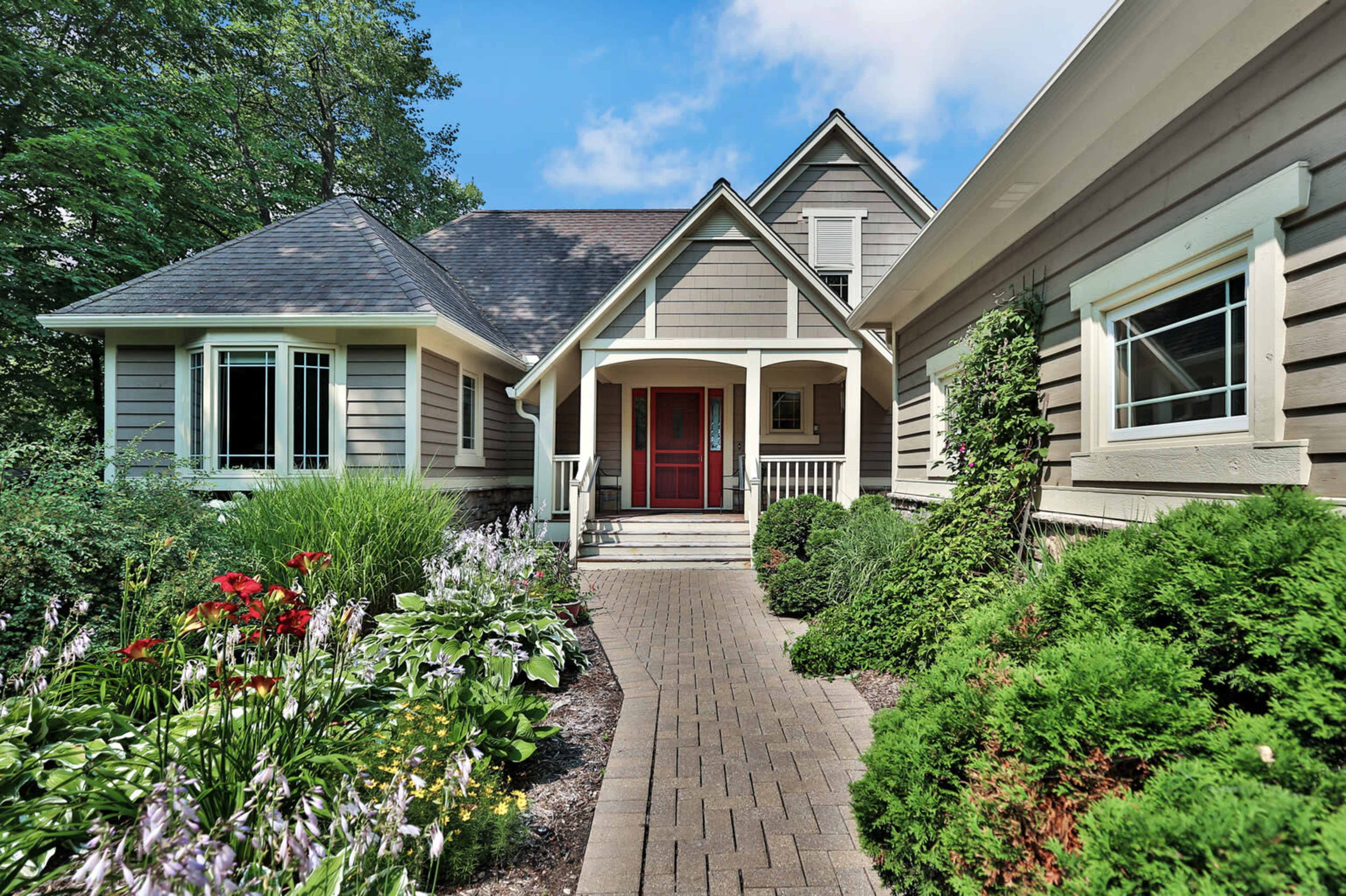 A well-landscaped pathway leads to the entrance of a modern home, framed by vibrant flower beds and greenery.