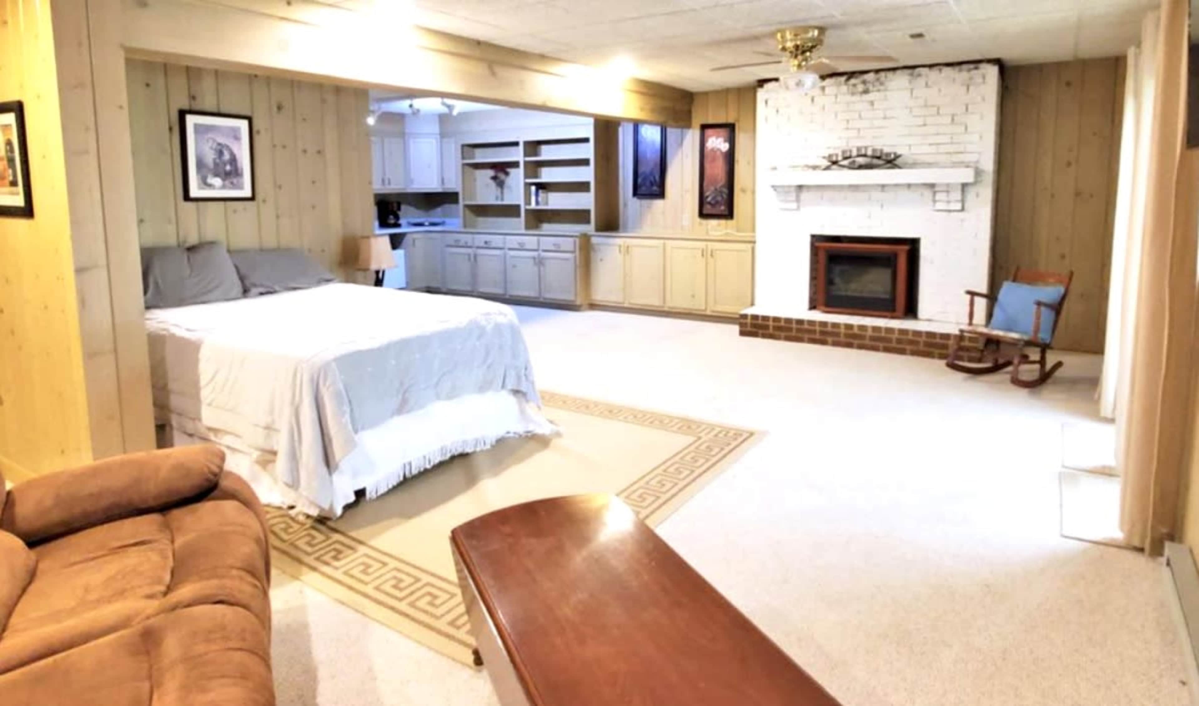 A spacious room with a bed, a fireplace, a sofa, and a kitchenette area with wooden cabinets.