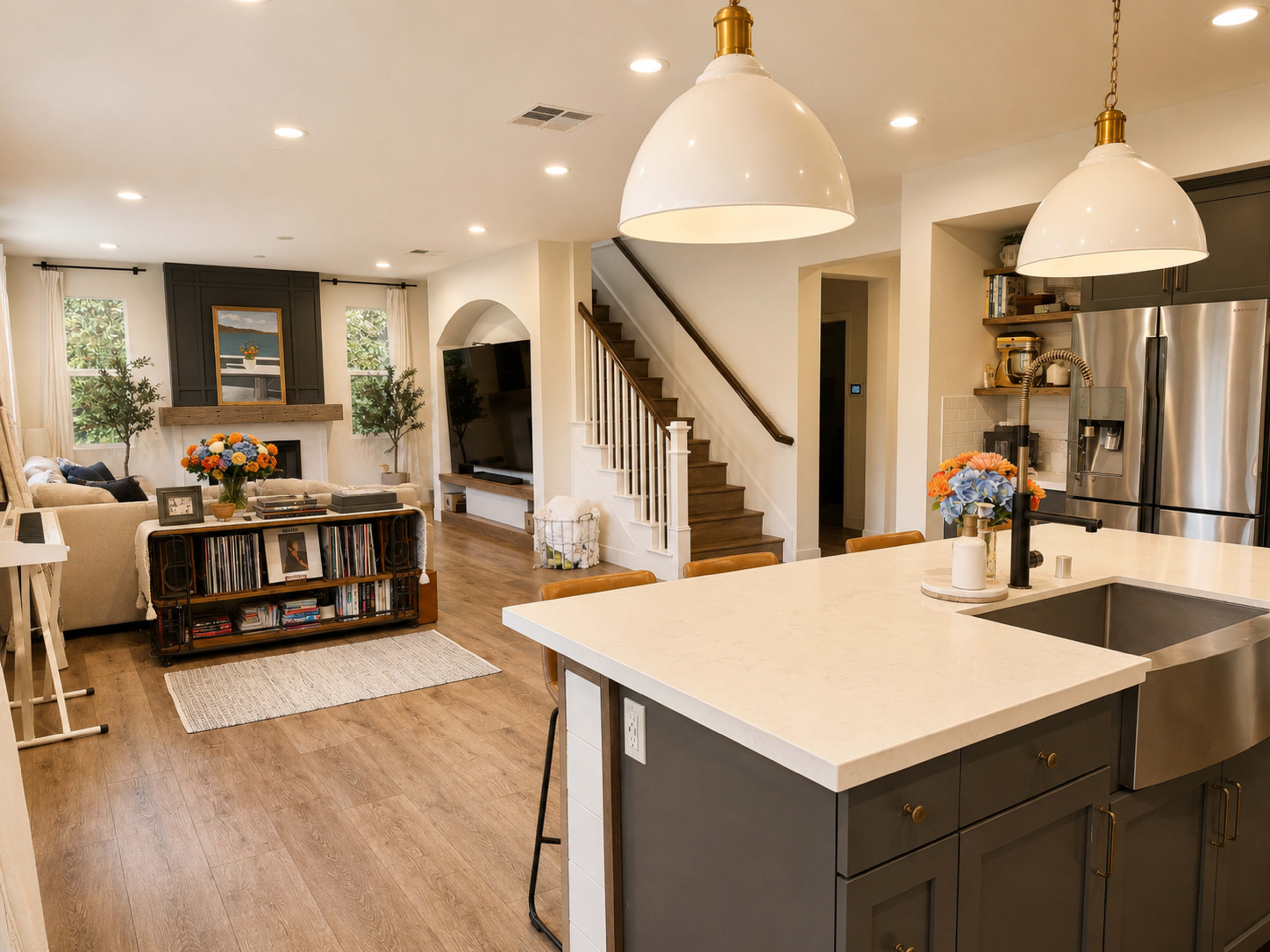 The image shows a modern open-concept living space featuring a kitchen with a large island, a dining area, and a living room with a sofa and a television.