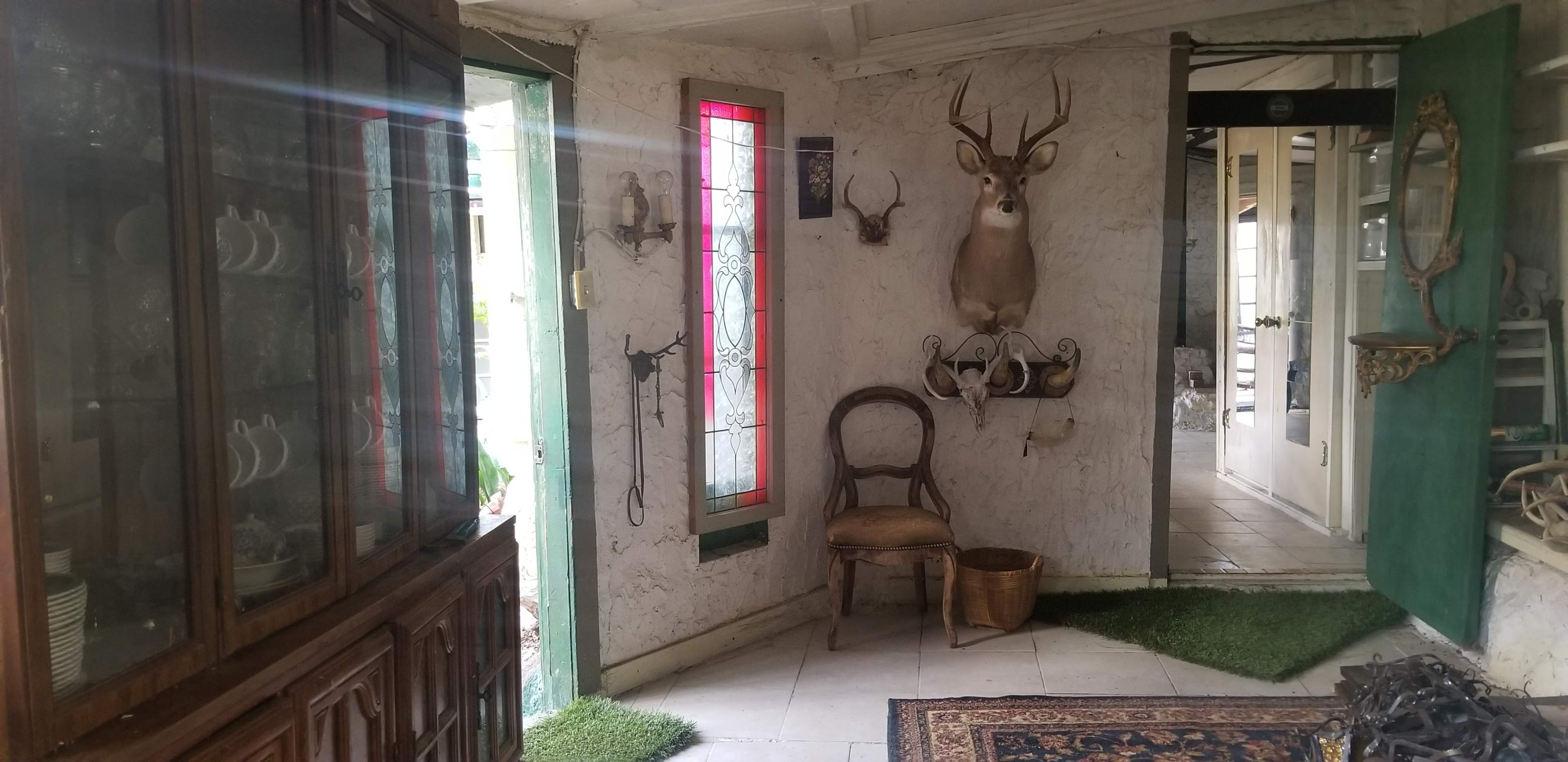An indoor entryway with a wooden cabinet, a deer mounted on the wall, and a chair next to a doorway leading outside.