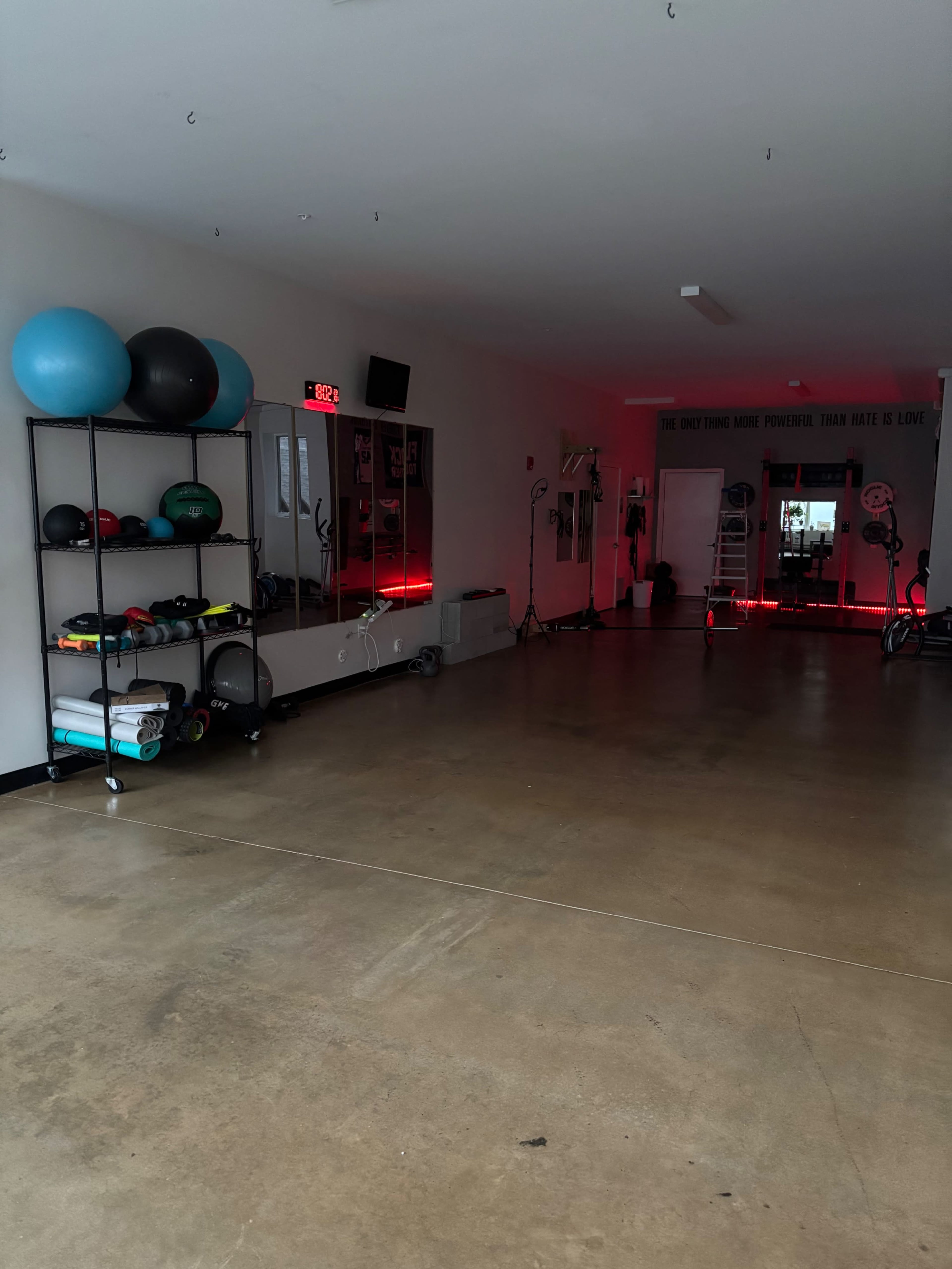 The image shows an empty gym space with various exercise equipment, including stability balls and weights on a shelf, while red lighting adds a distinct ambiance.