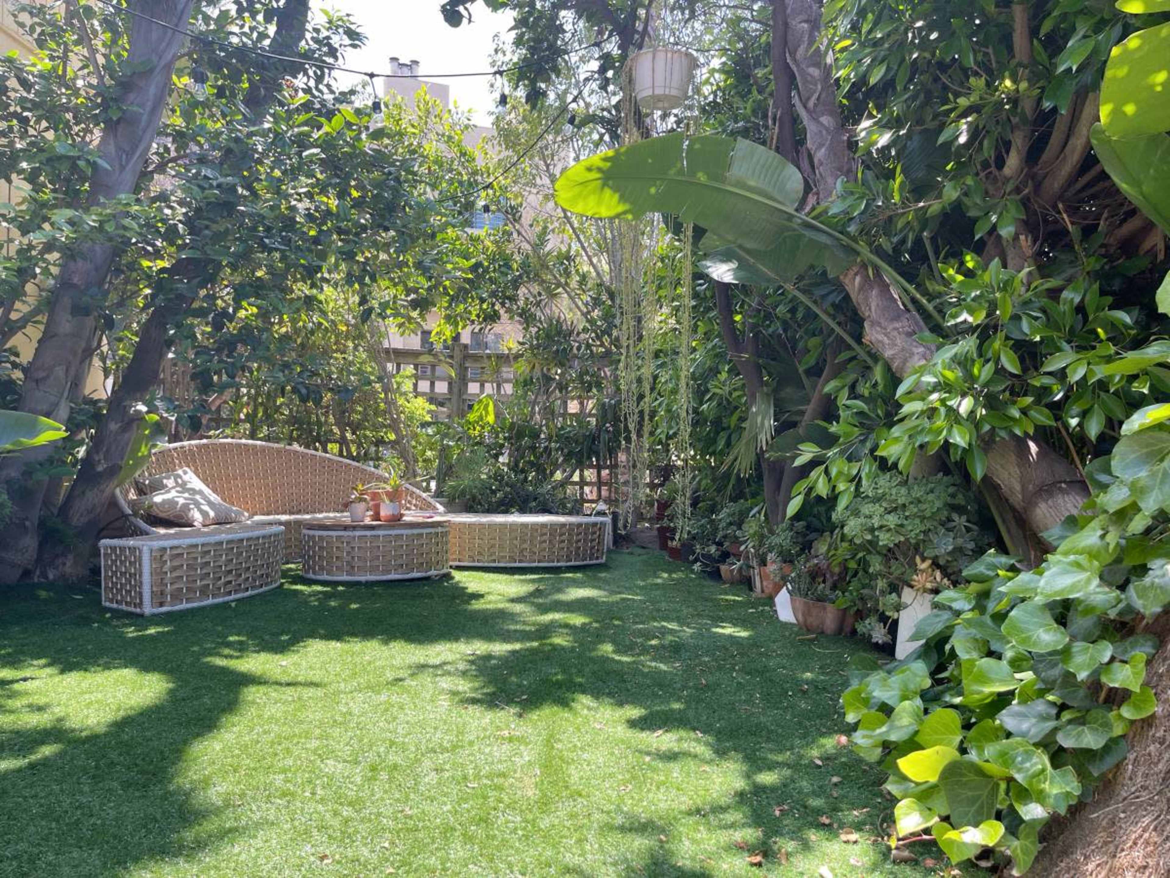 A small outdoor seating area surrounded by lush greenery and potted plants on artificial grass.