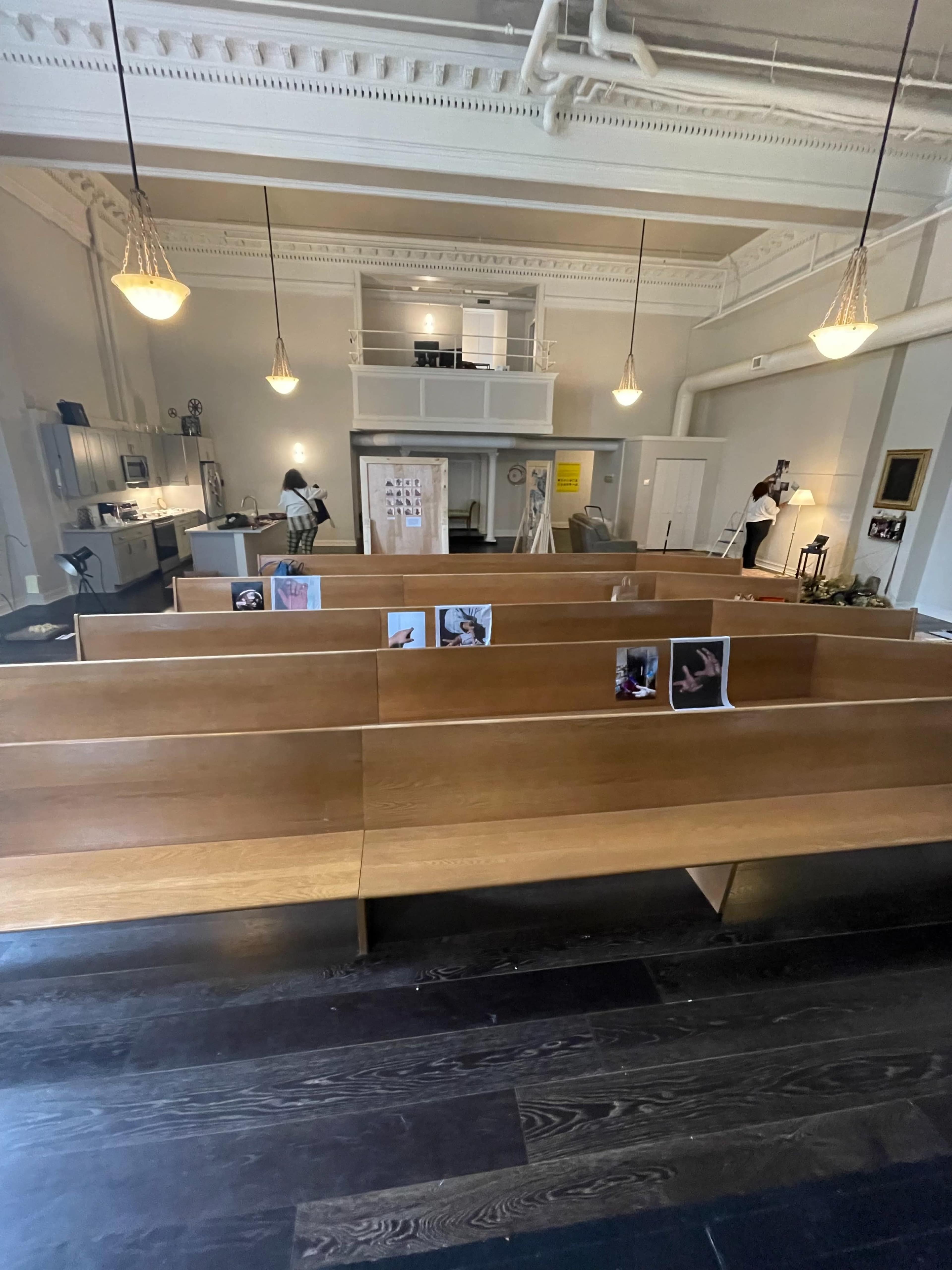 A spacious interior with wooden pew-like benches facing a modern kitchen and art display area.