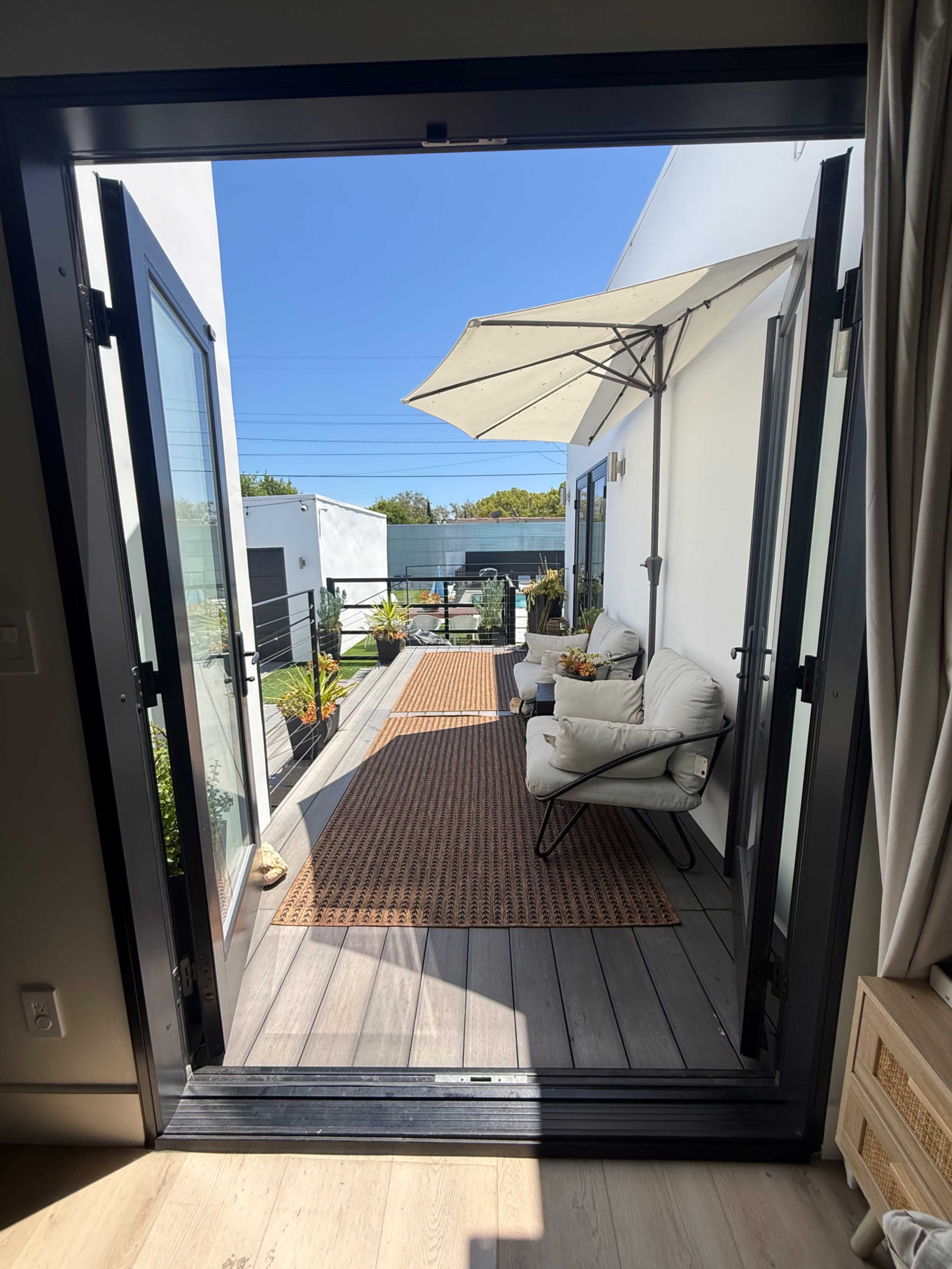 A spacious terrace with outdoor seating, an umbrella, and potted plants, viewed through open double doors.