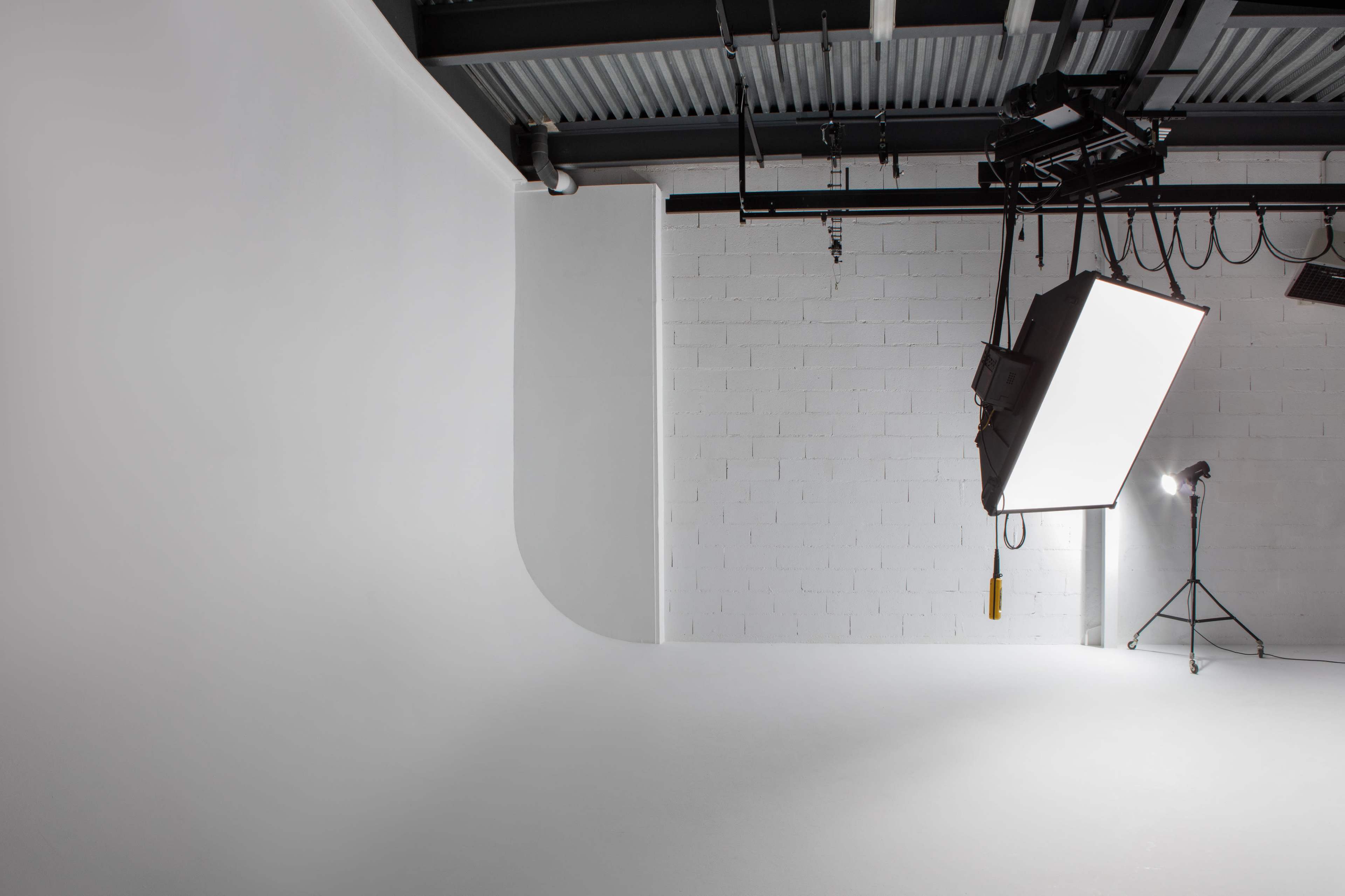 A minimalist photography studio with a seamless white backdrop and lighting equipment mounted from the ceiling.