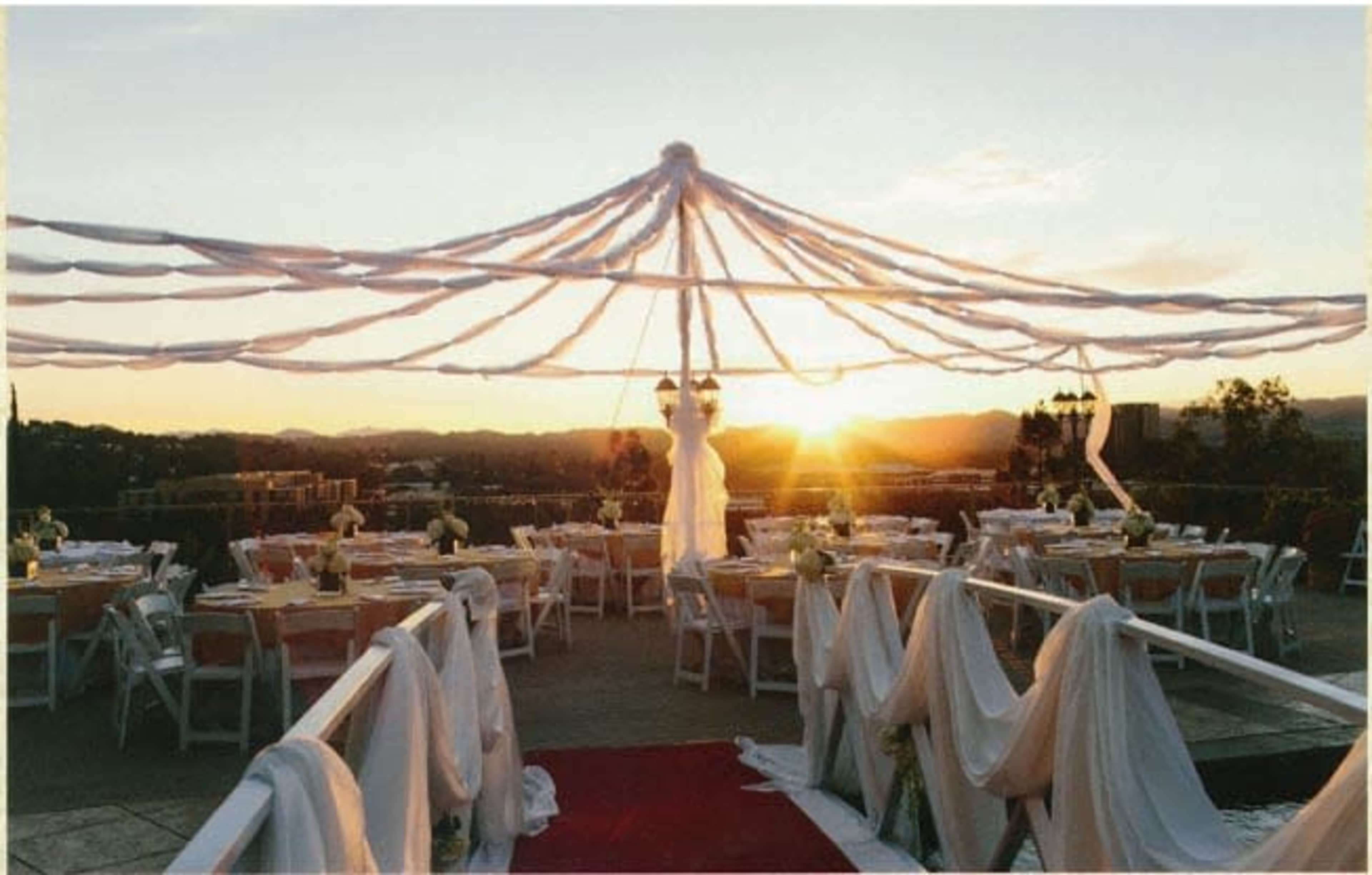A decorated outdoor wedding venue features a large canopy and tables arranged for a sunset ceremony.