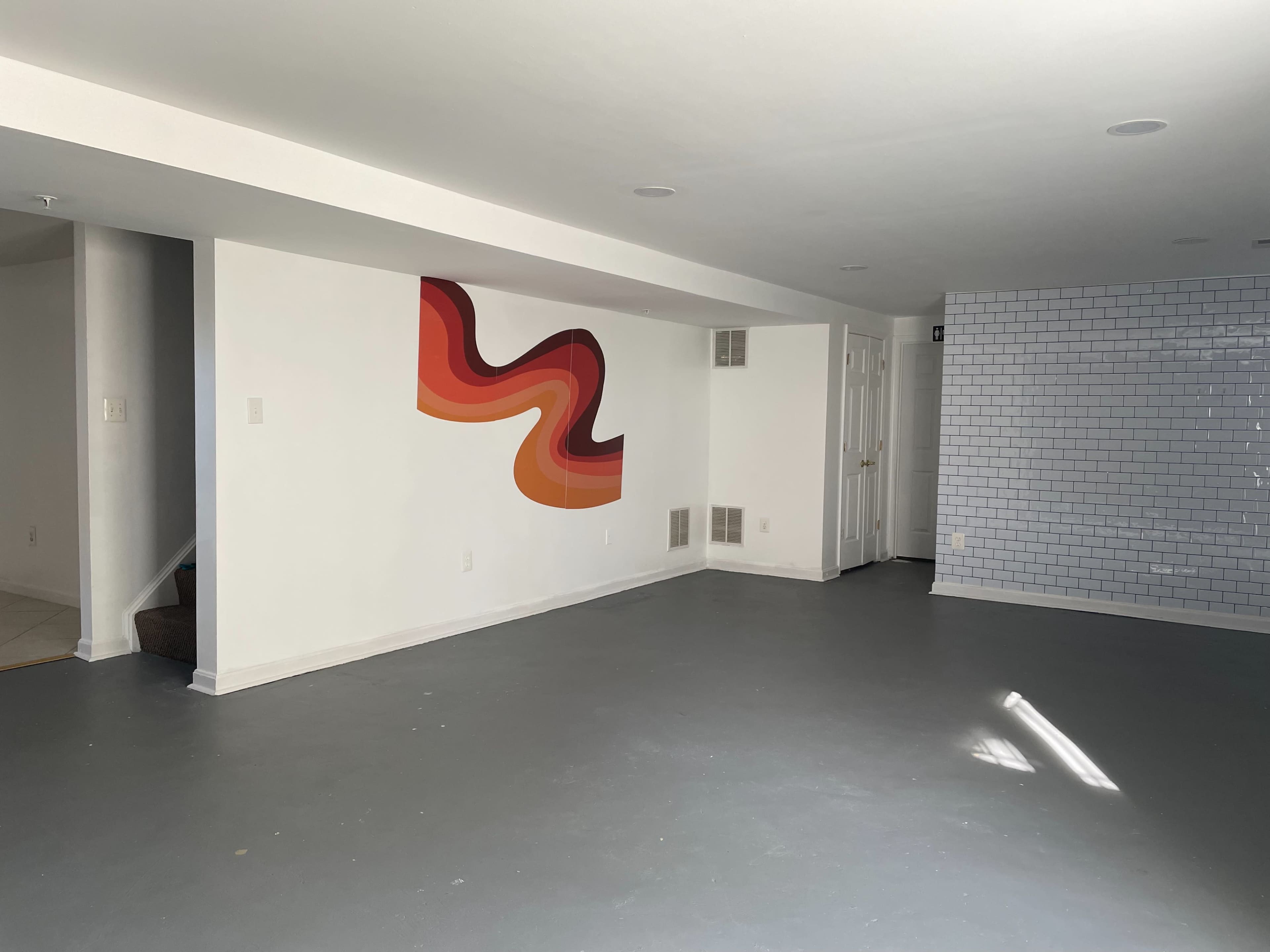 A spacious, empty room with a colorful mural on one wall and a tiled wall on the opposite side.