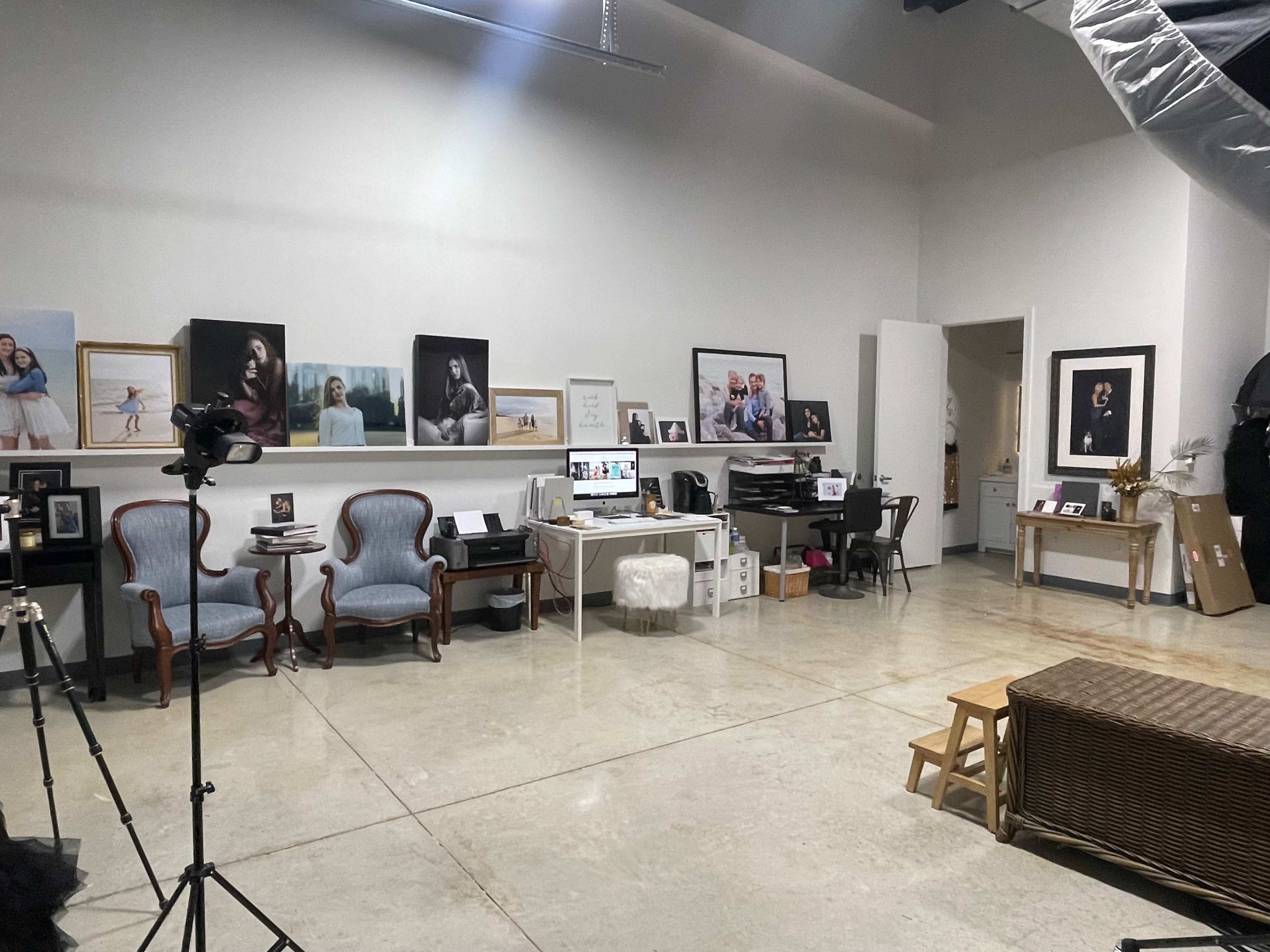 A studio space with two blue chairs, a desk with a computer, framed photographs on the walls, and various furnishings.