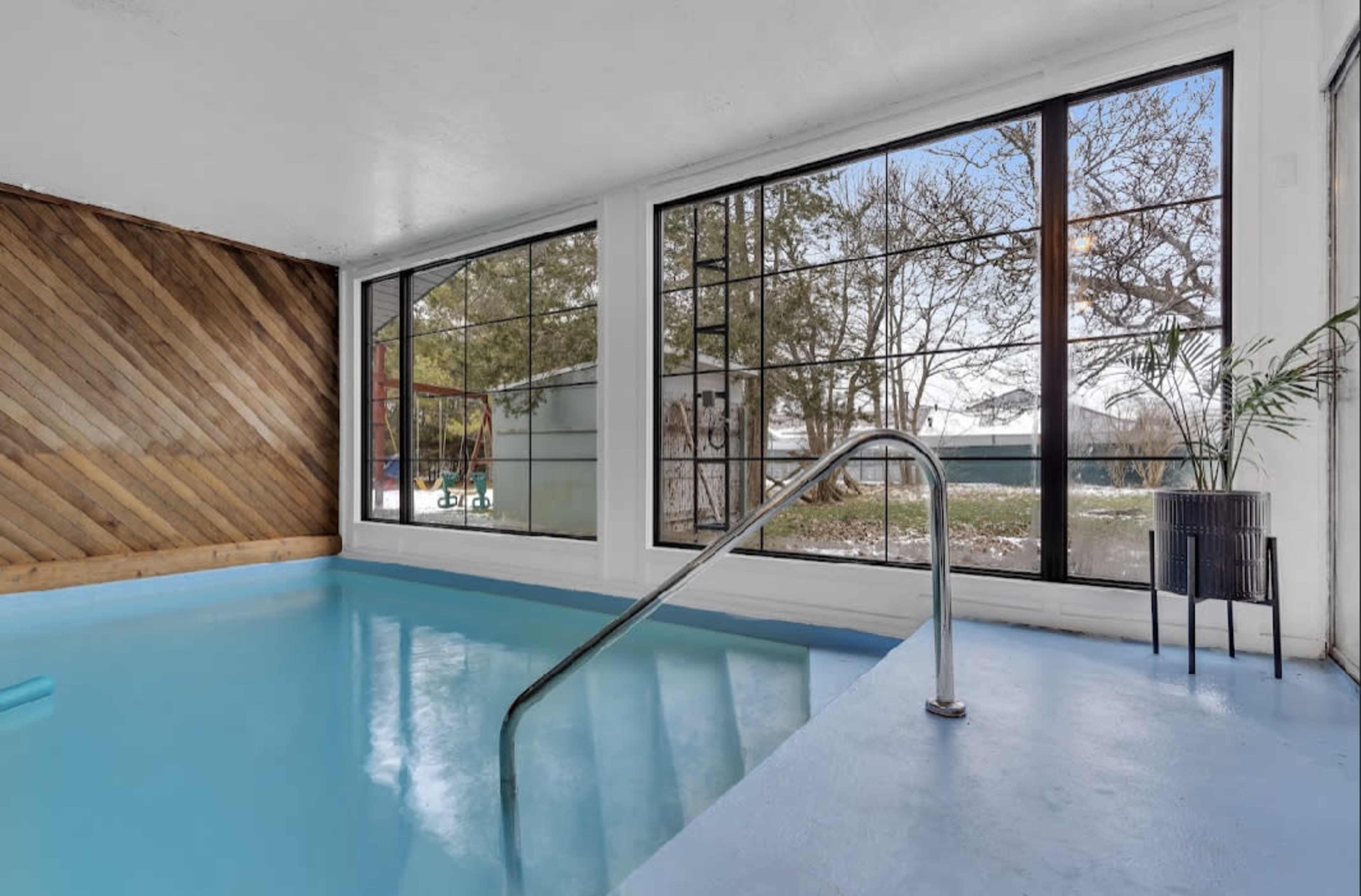 An indoor swimming pool with large windows overlooking a yard.
