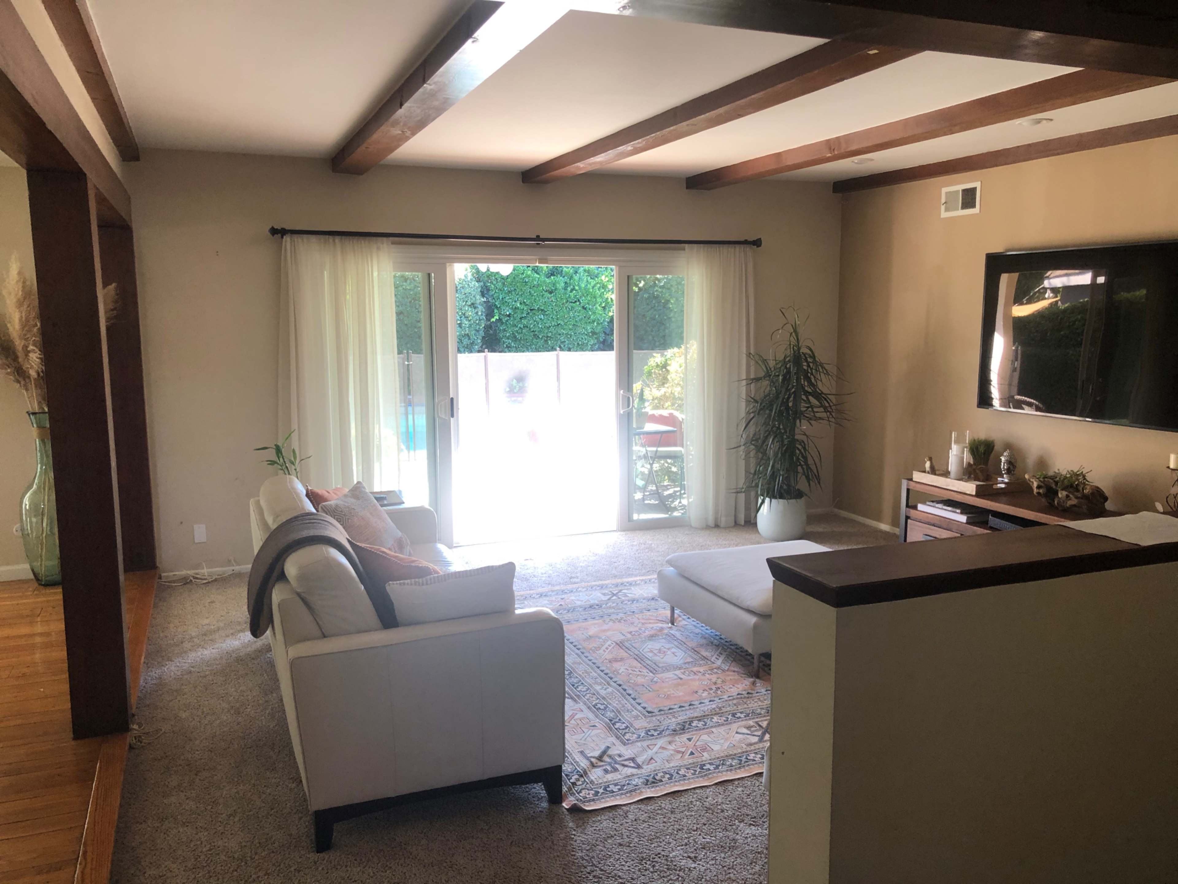 The room features a white sofa and a decorative rug, with large glass doors leading to a patio area visible through the sheer curtains.