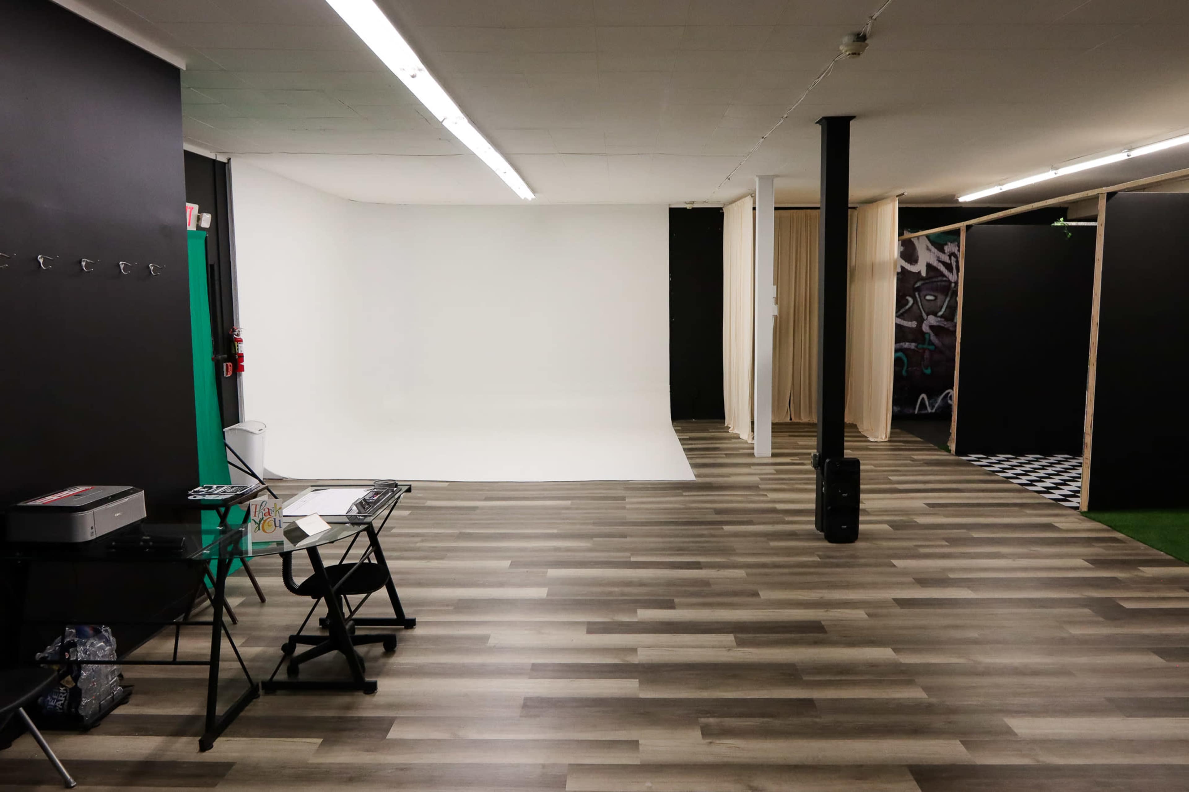 A spacious studio or gallery with a white backdrop on one side, wooden flooring, and various partitions and equipment visible.