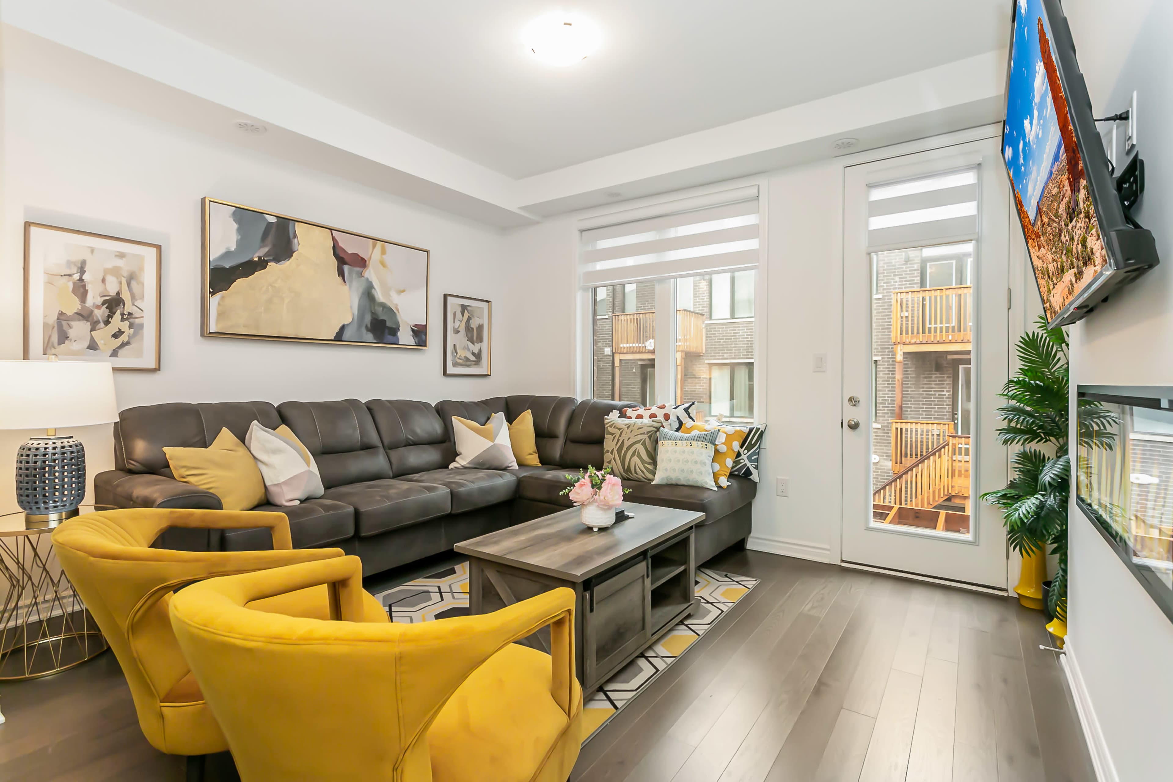 The living room features a large sectional sofa, two yellow chairs, a coffee table, and a door leading to a balcony.