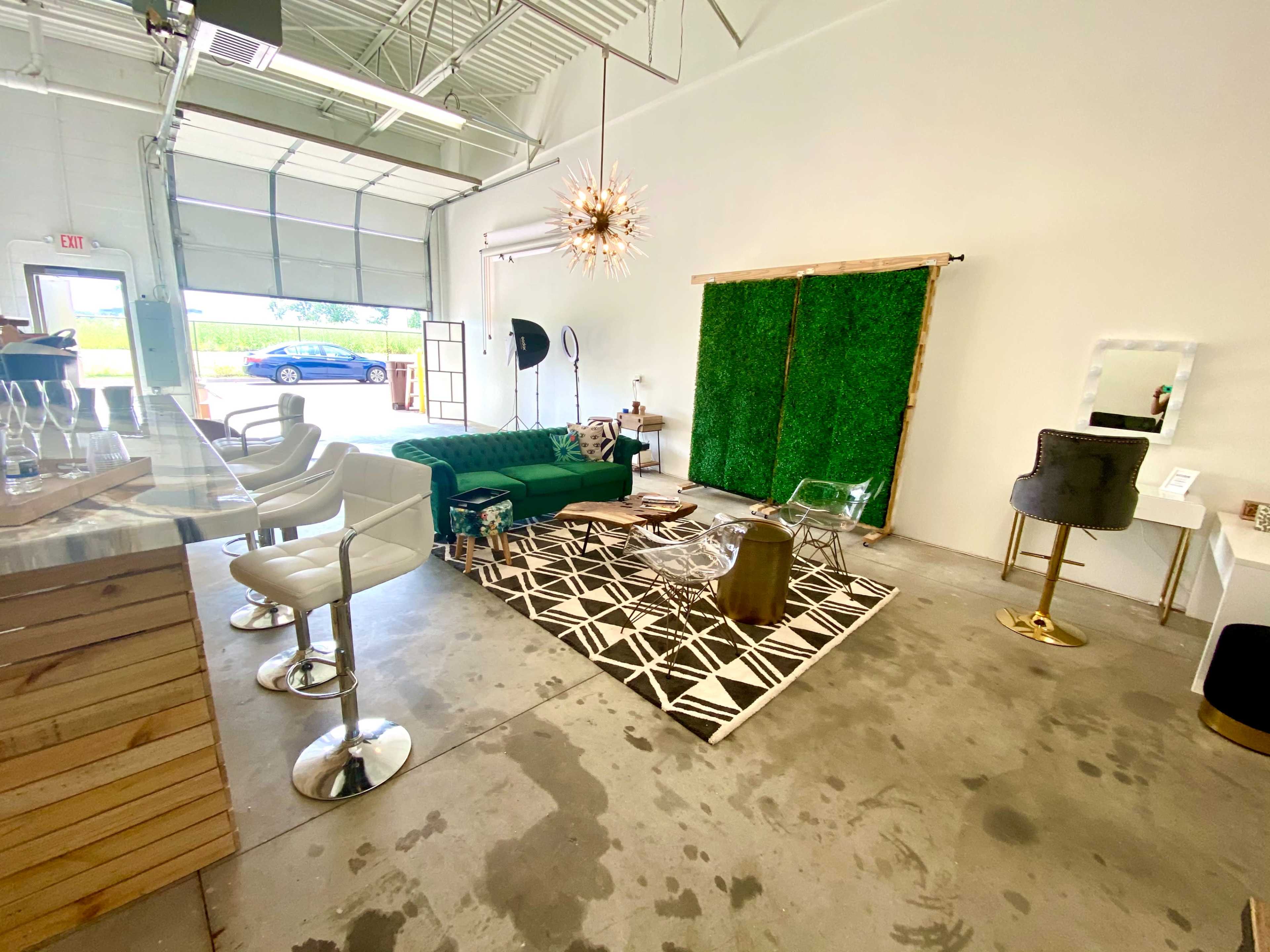 A modern interior space with a green sofa, a geometric rug, a lounge area with clear chairs, and a decorative wall made of greenery.