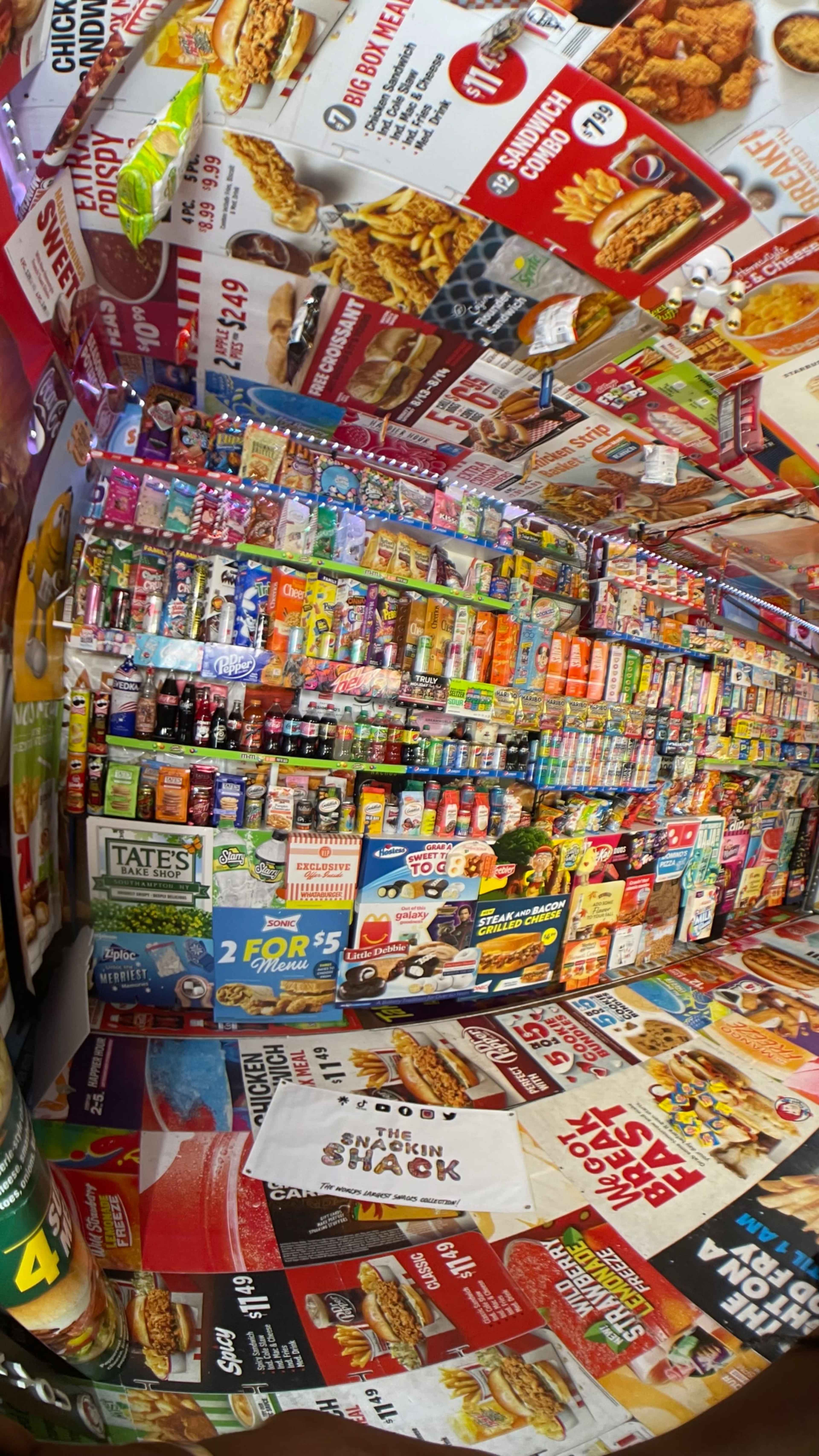 The image displays an interior filled with colorful food packaging and advertisements covering the walls, ceiling, and floor.