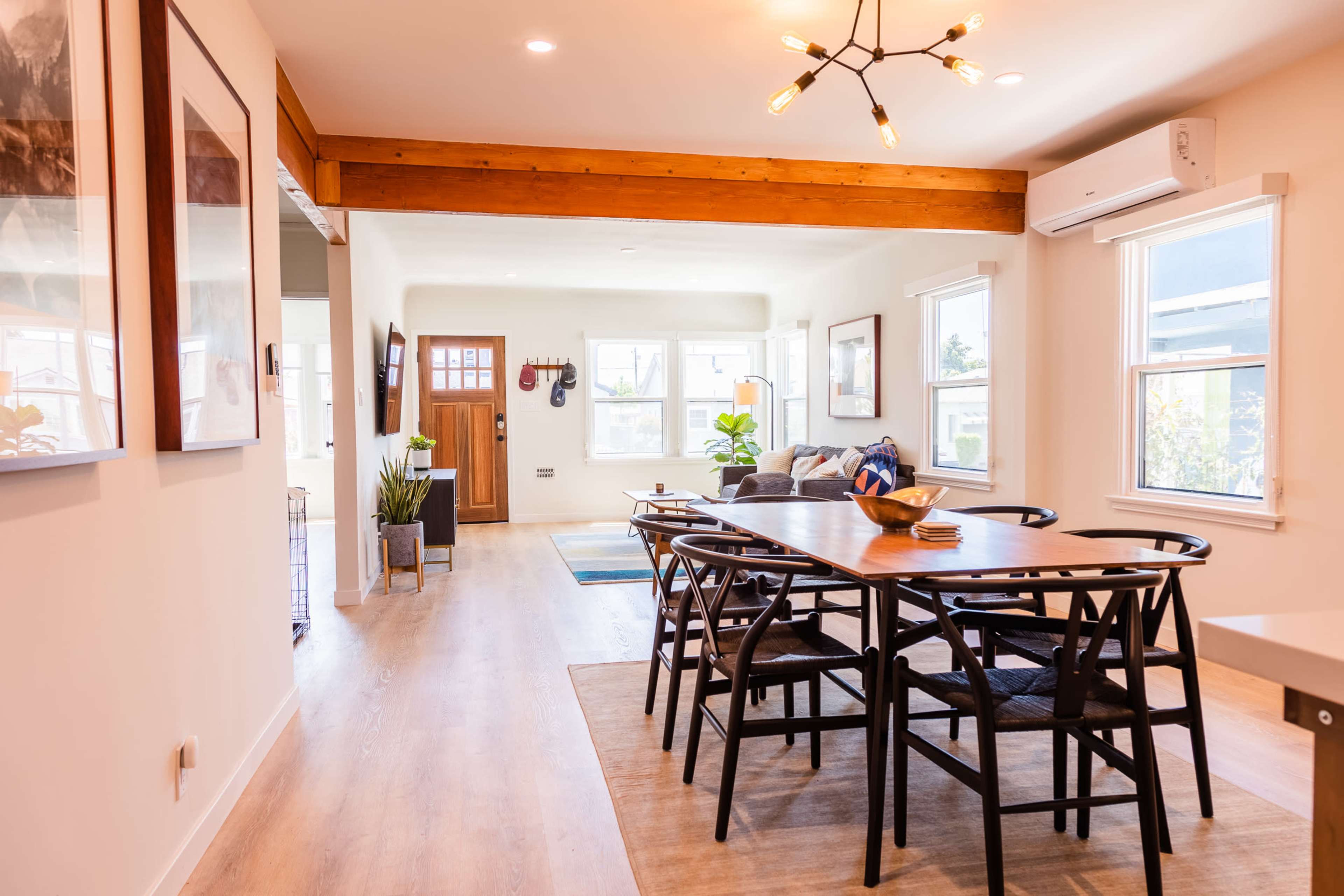 A dining area features a wooden table surrounded by chairs, with a view of a living space and a doorway in the background.