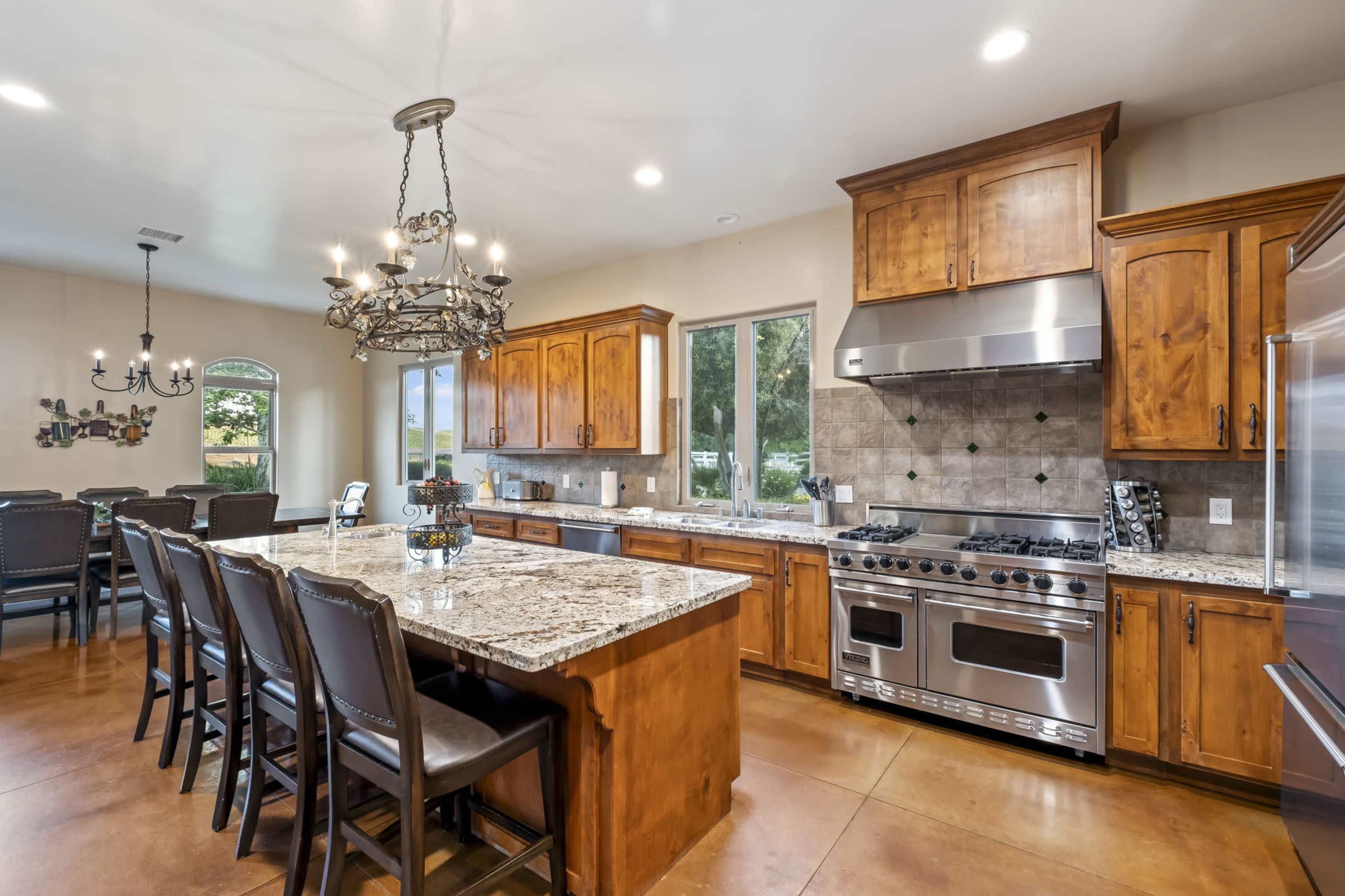 A spacious kitchen features wooden cabinetry, a large granite island with seating, and stainless steel appliances.