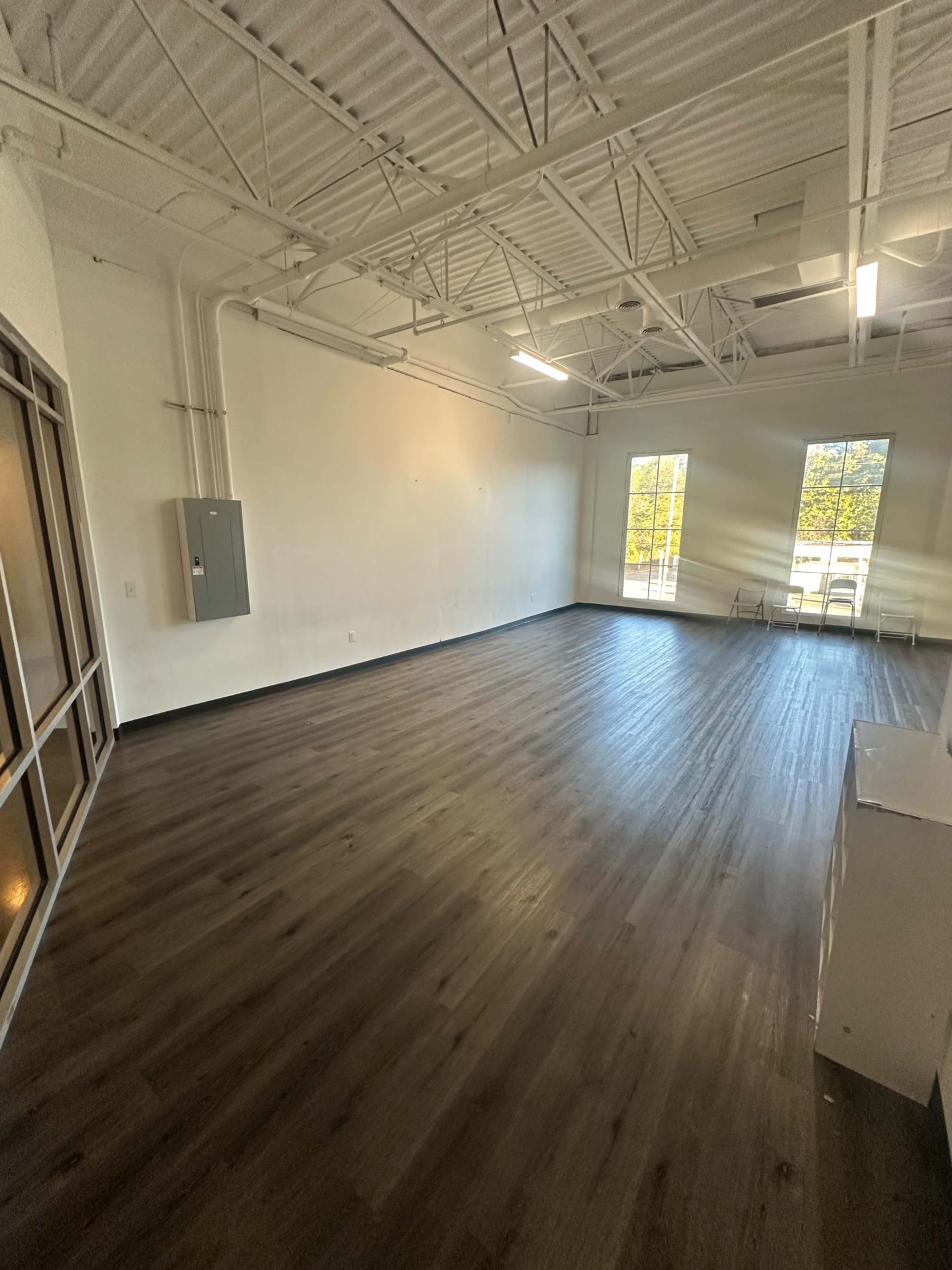 The image shows an empty room with new wooden flooring, white walls, and two large windows allowing natural light.