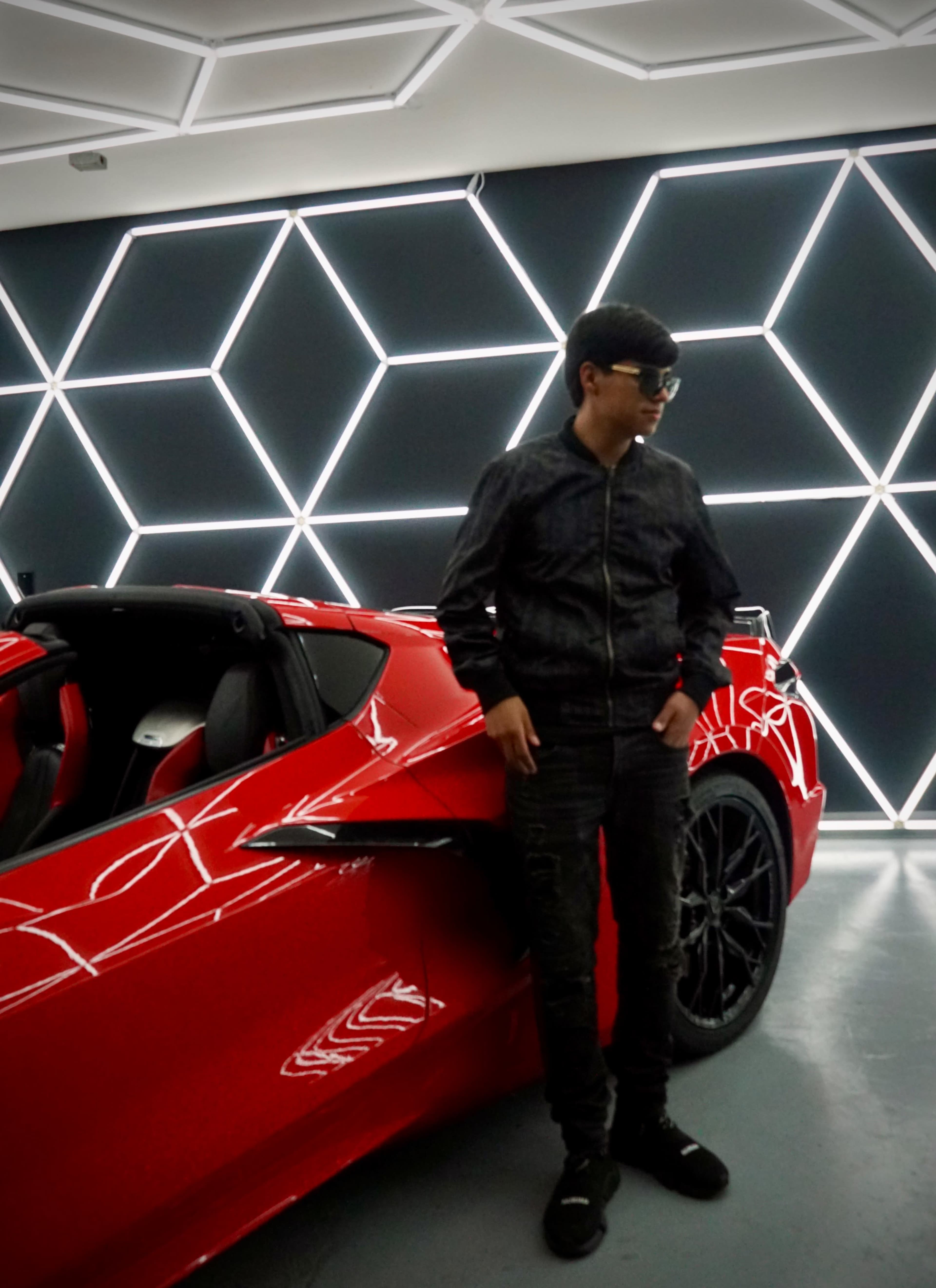 A person stands beside a red sports car in a modern room with geometric lighting.