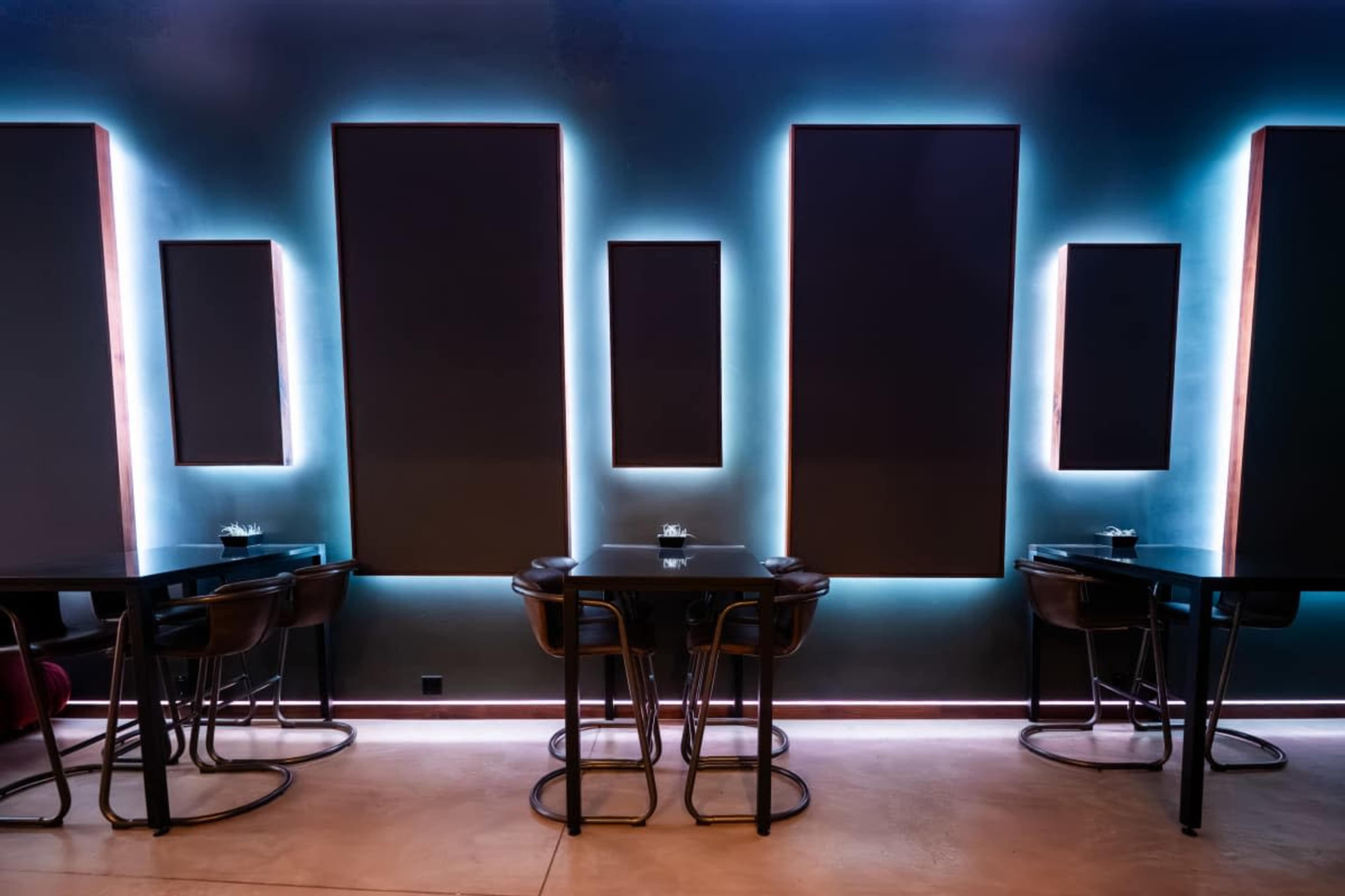 The image shows a modern interior of a restaurant or cafe featuring black seating with tables and illuminated rectangular wall panels.