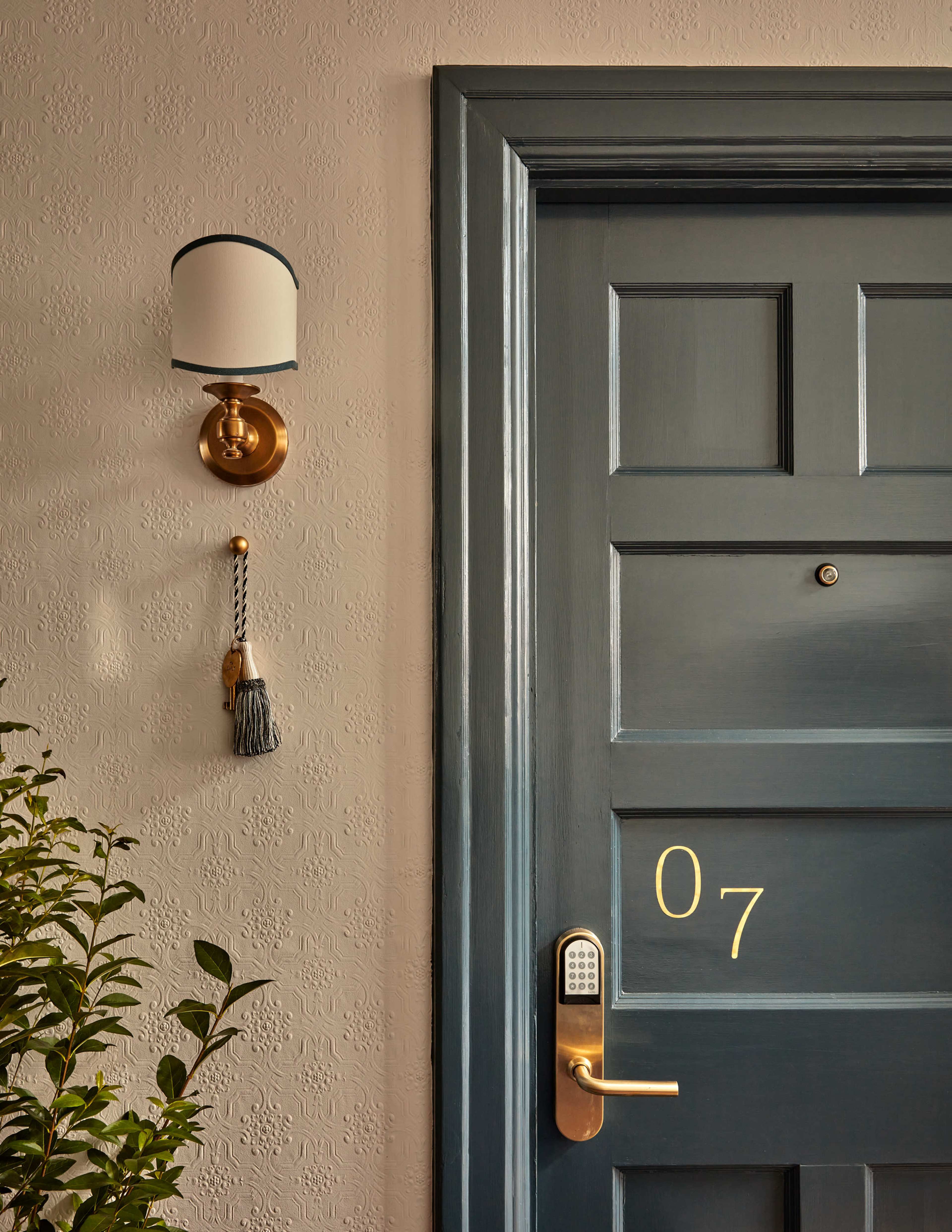 A blue door with the number 07, a wall-mounted sconce, and a decorative tassel beside it.