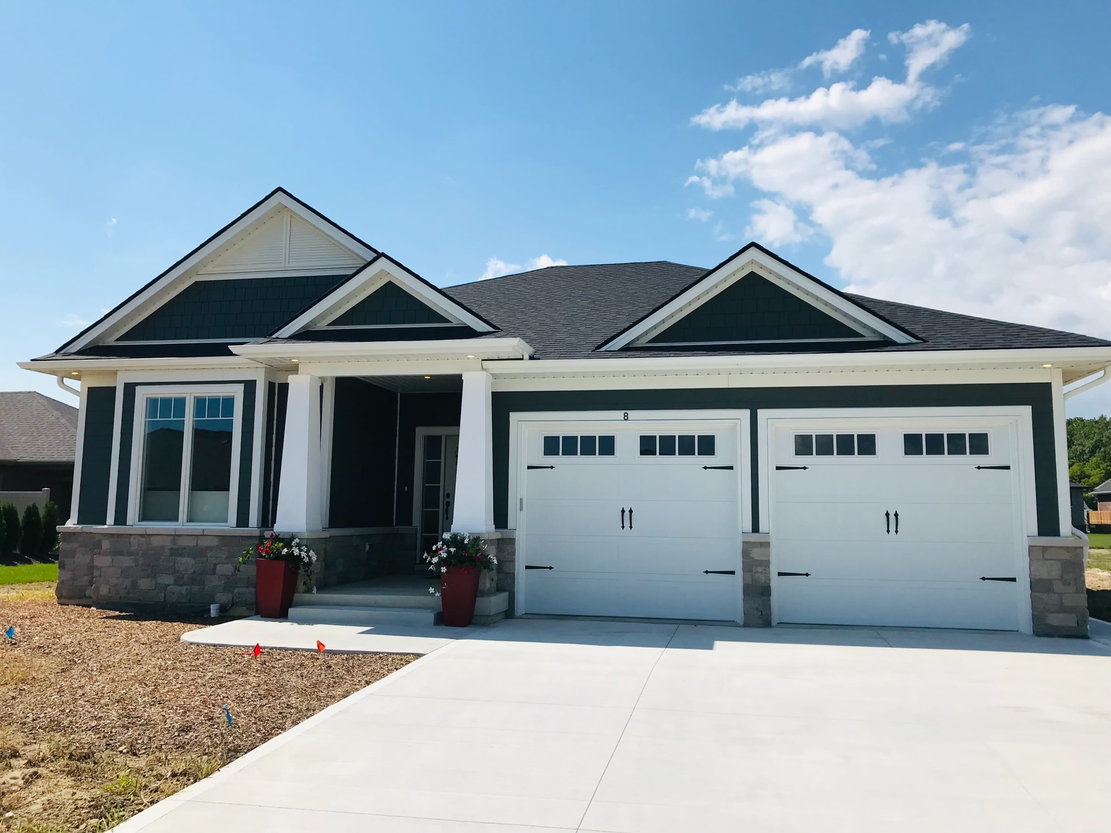 A single-story house with a dark exterior, two garage doors, and a front porch featuring planters.