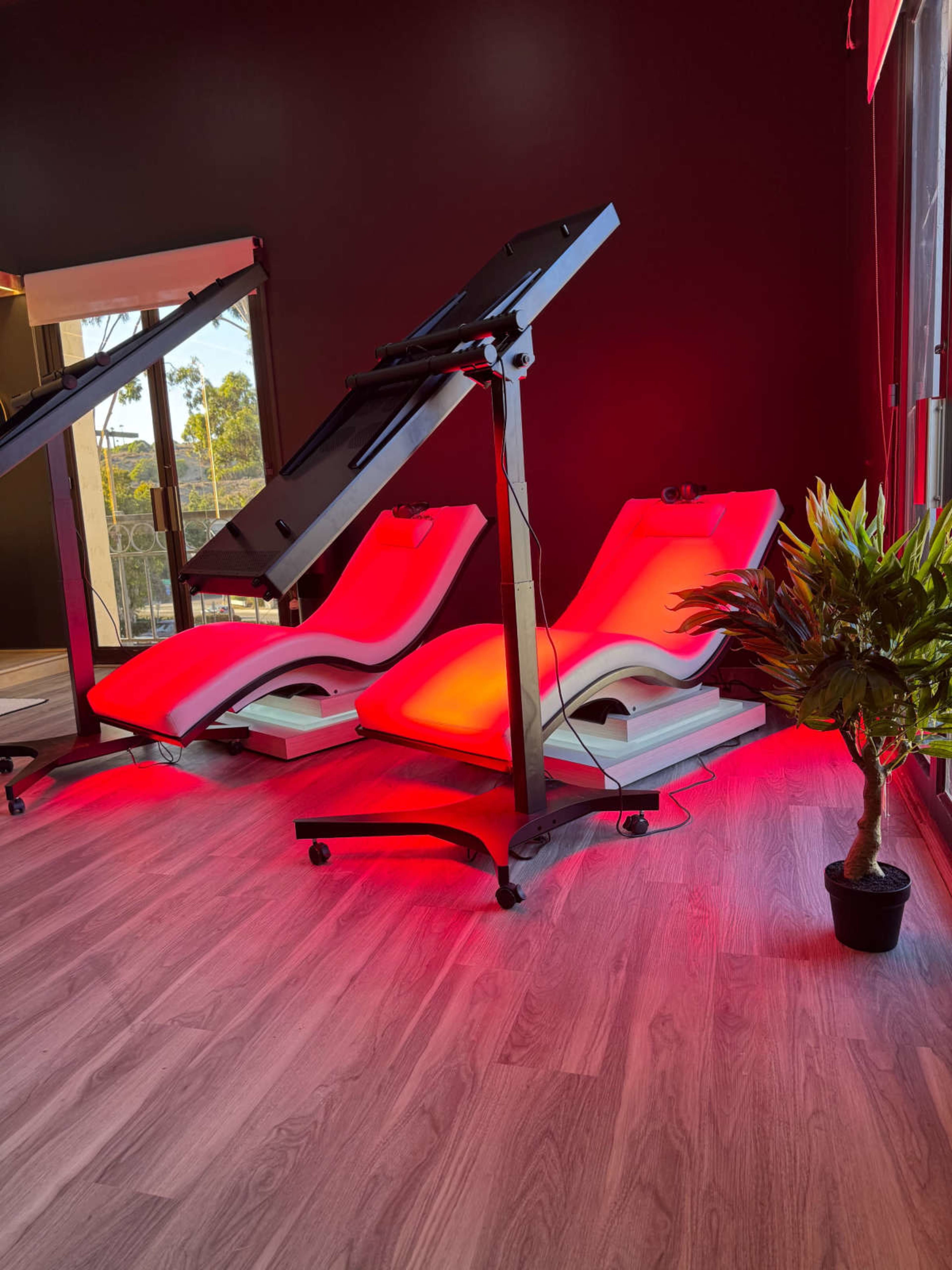 The image shows two red-lit therapy beds positioned in a room with dark walls and a large mirror.
