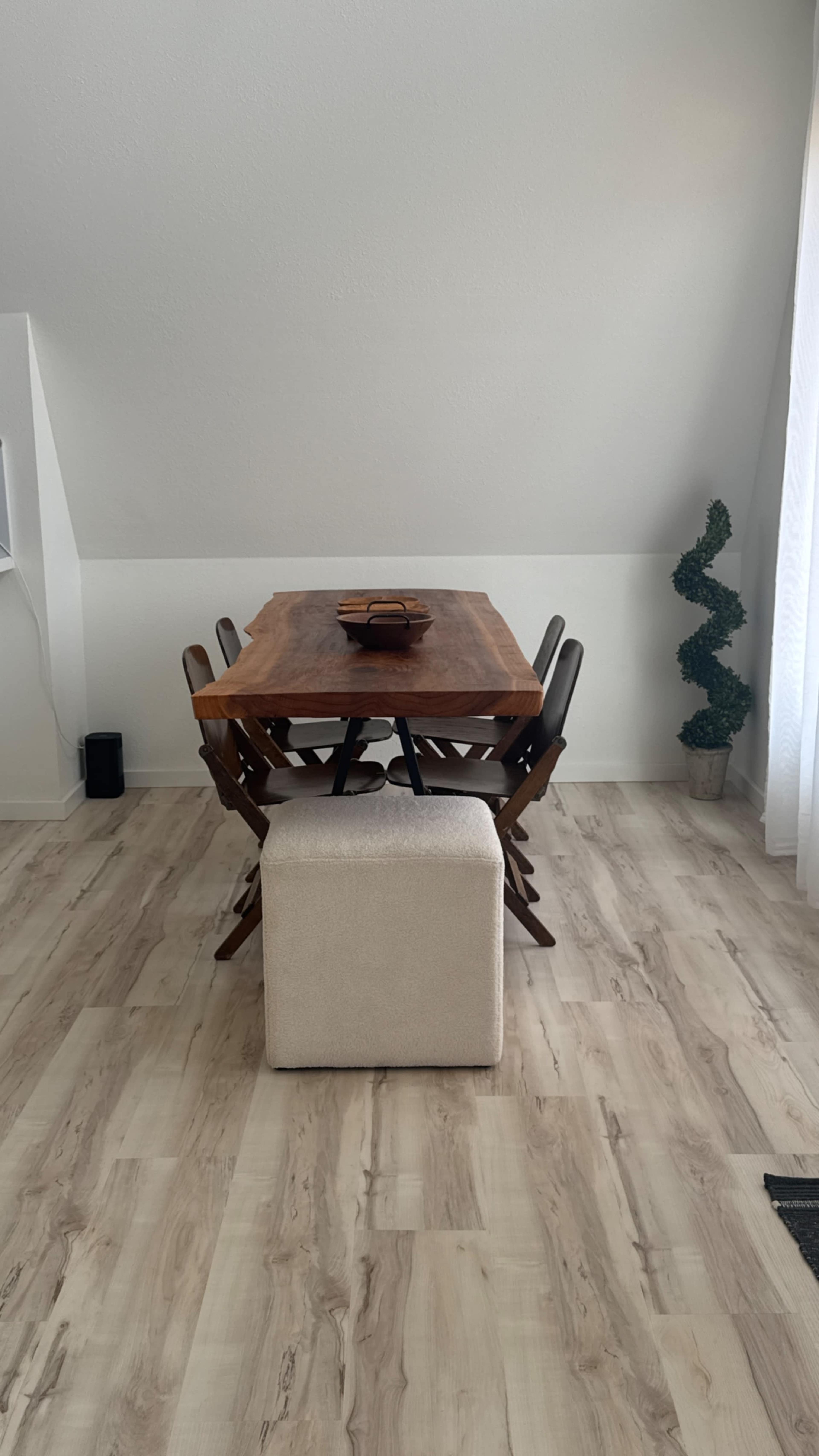 A wooden dining table is set in a light-colored room with four chairs and a decorative plant in the corner.