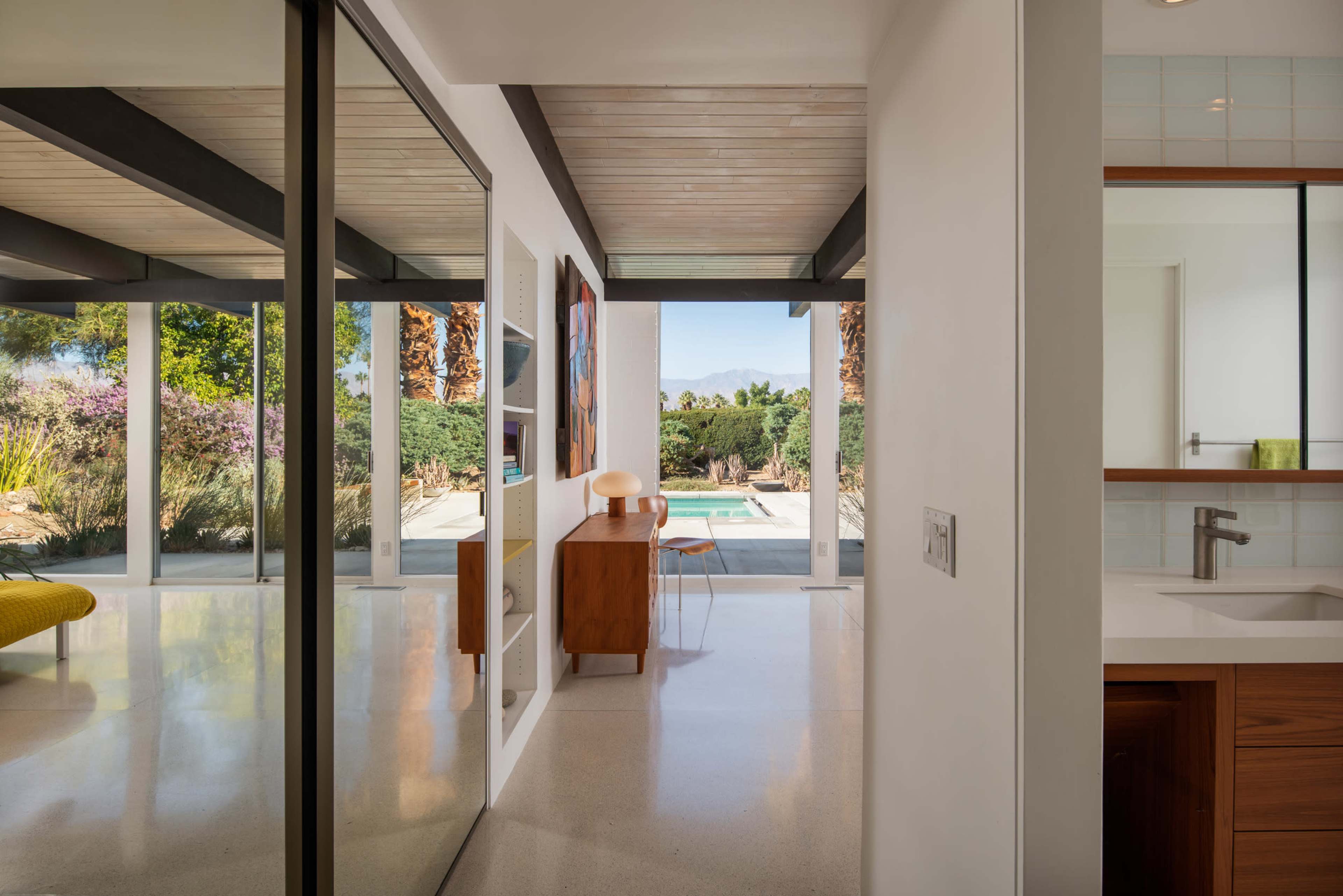 A modern interior showcases a view of a pool and landscaped yard through large glass doors, with contemporary furniture and art lining the walls.