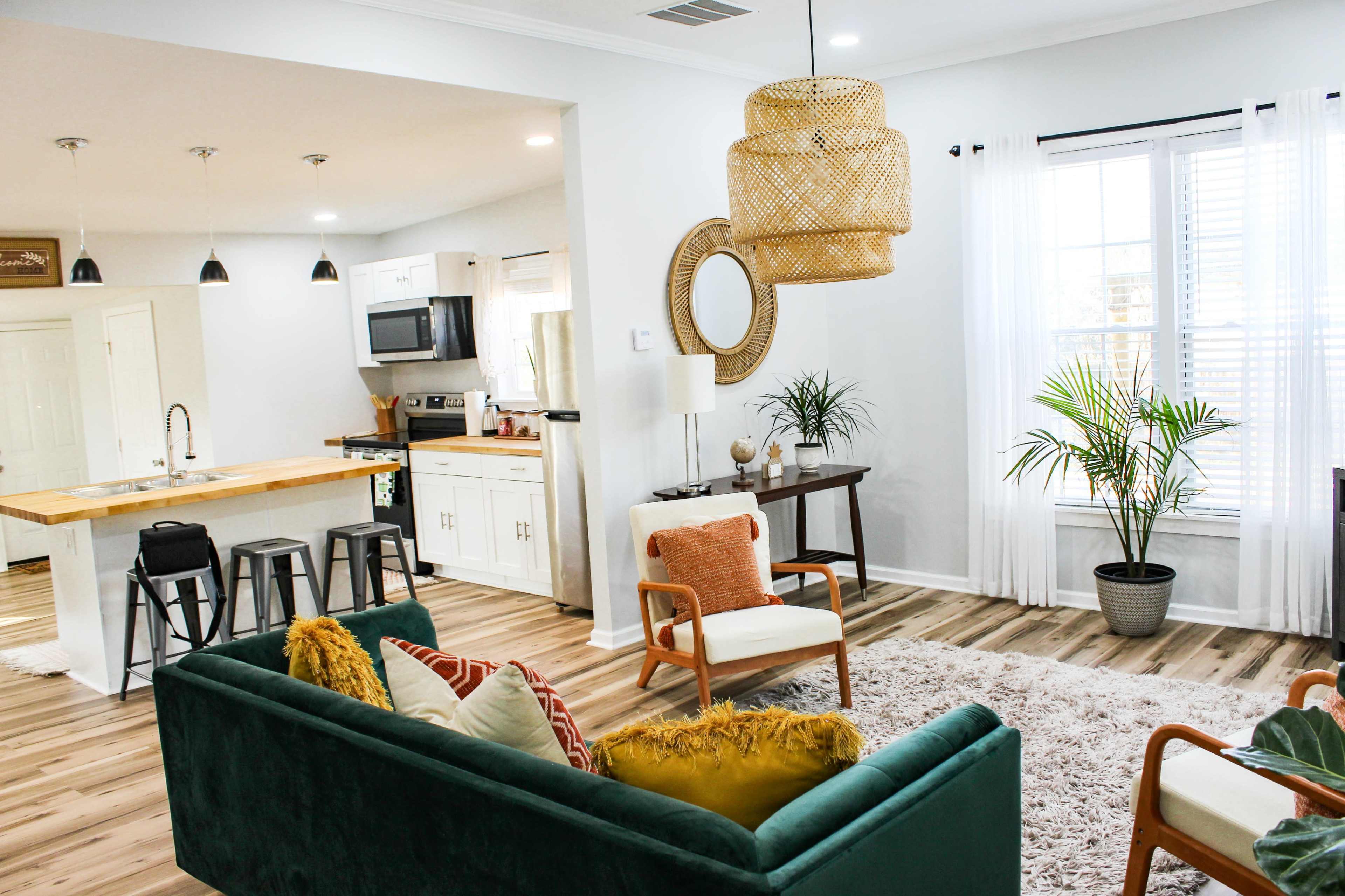 A modern living space featuring a green sofa, a wooden dining area, and large windows with plants.