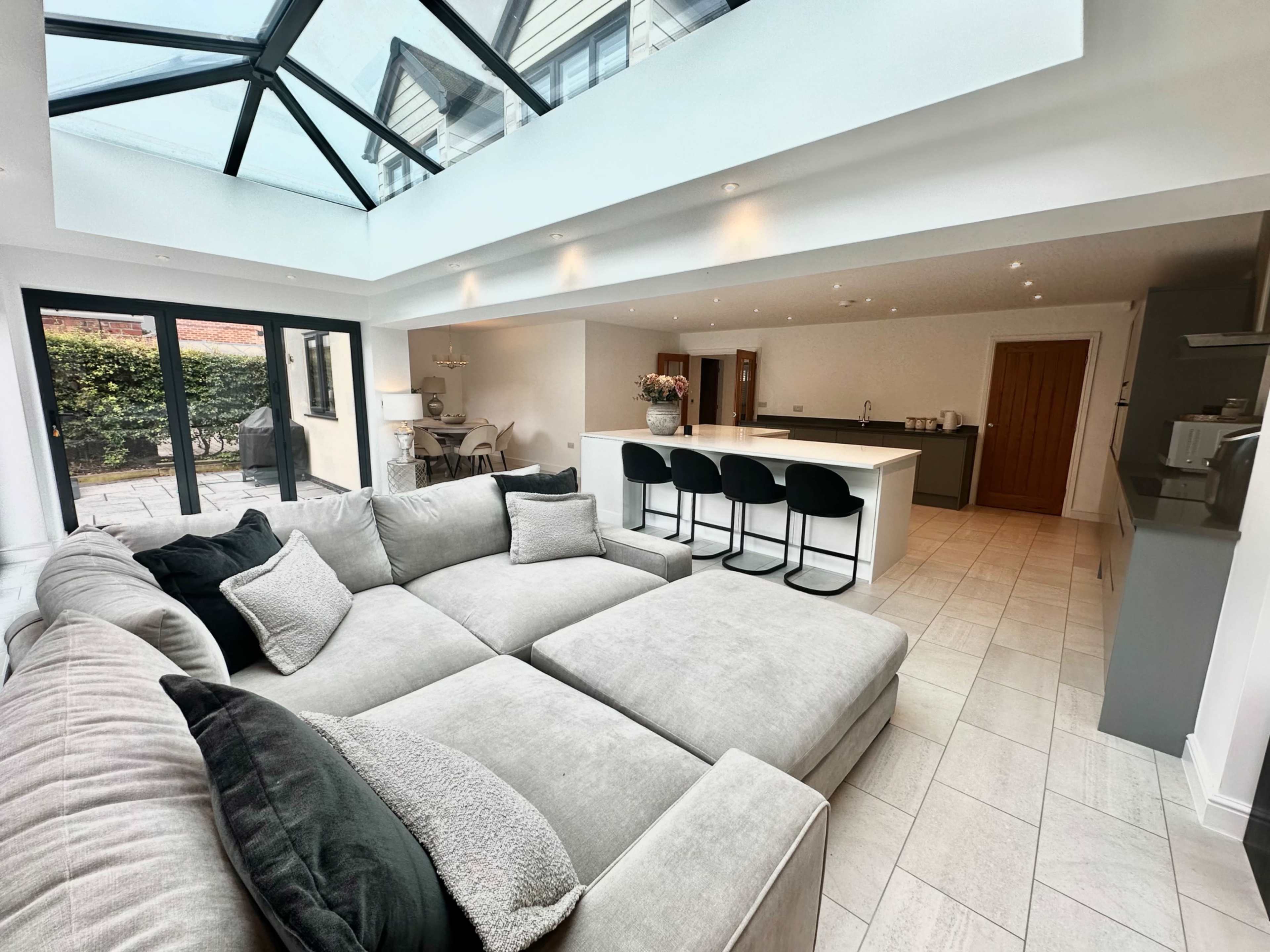 A modern living space with a plush gray sectional sofa, a large island kitchen, and a glass ceiling that allows natural light to fill the area.