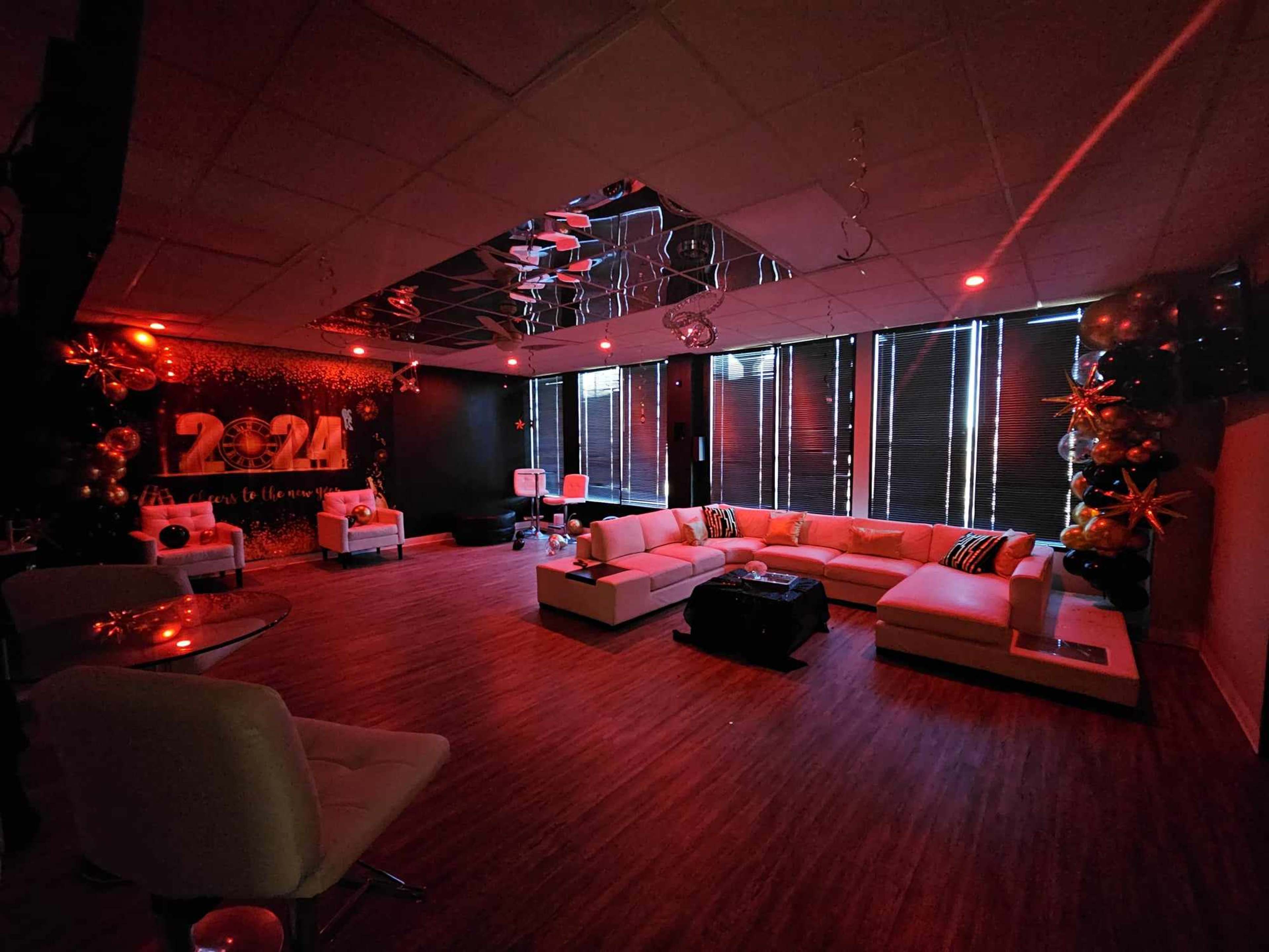A lounge area with a large sectional sofa, a glass table, and red lighting, featuring decorative balloons and mirrors on the walls.