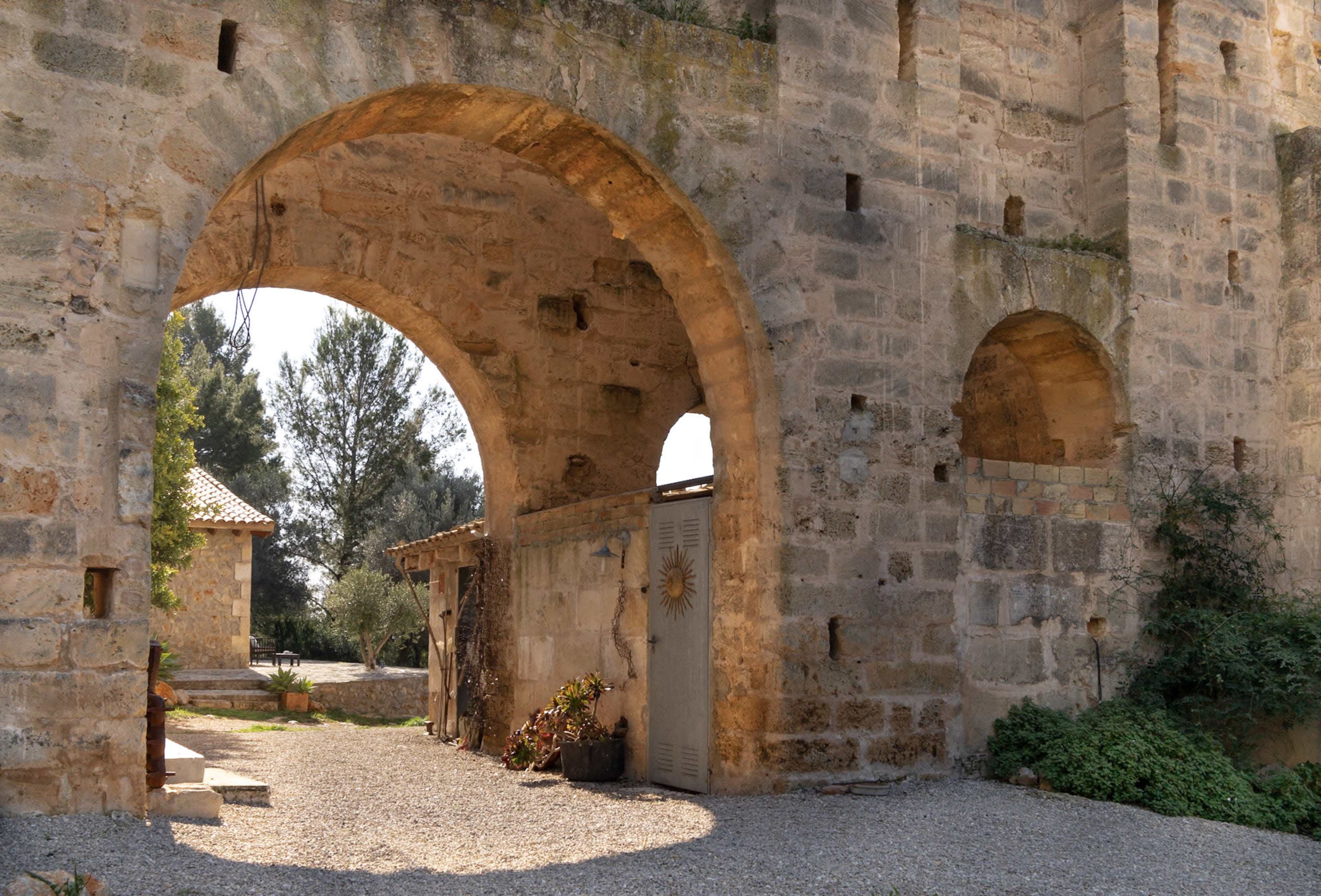 The image shows a stone archway leading to a courtyard, surrounded by ancient walls and greenery.