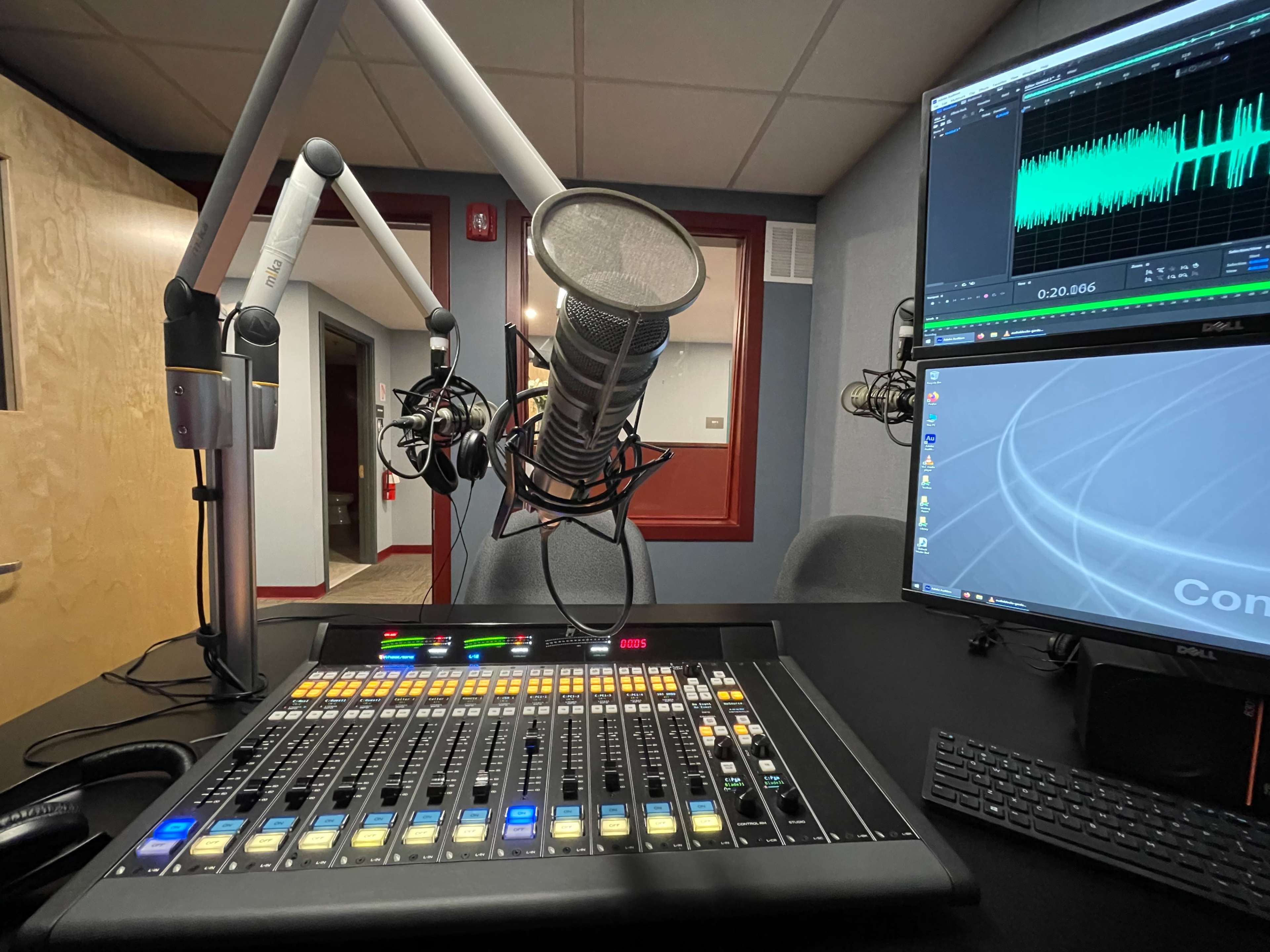 A radio studio setup with a microphone, mixing console, and computer monitors displaying sound waveforms.