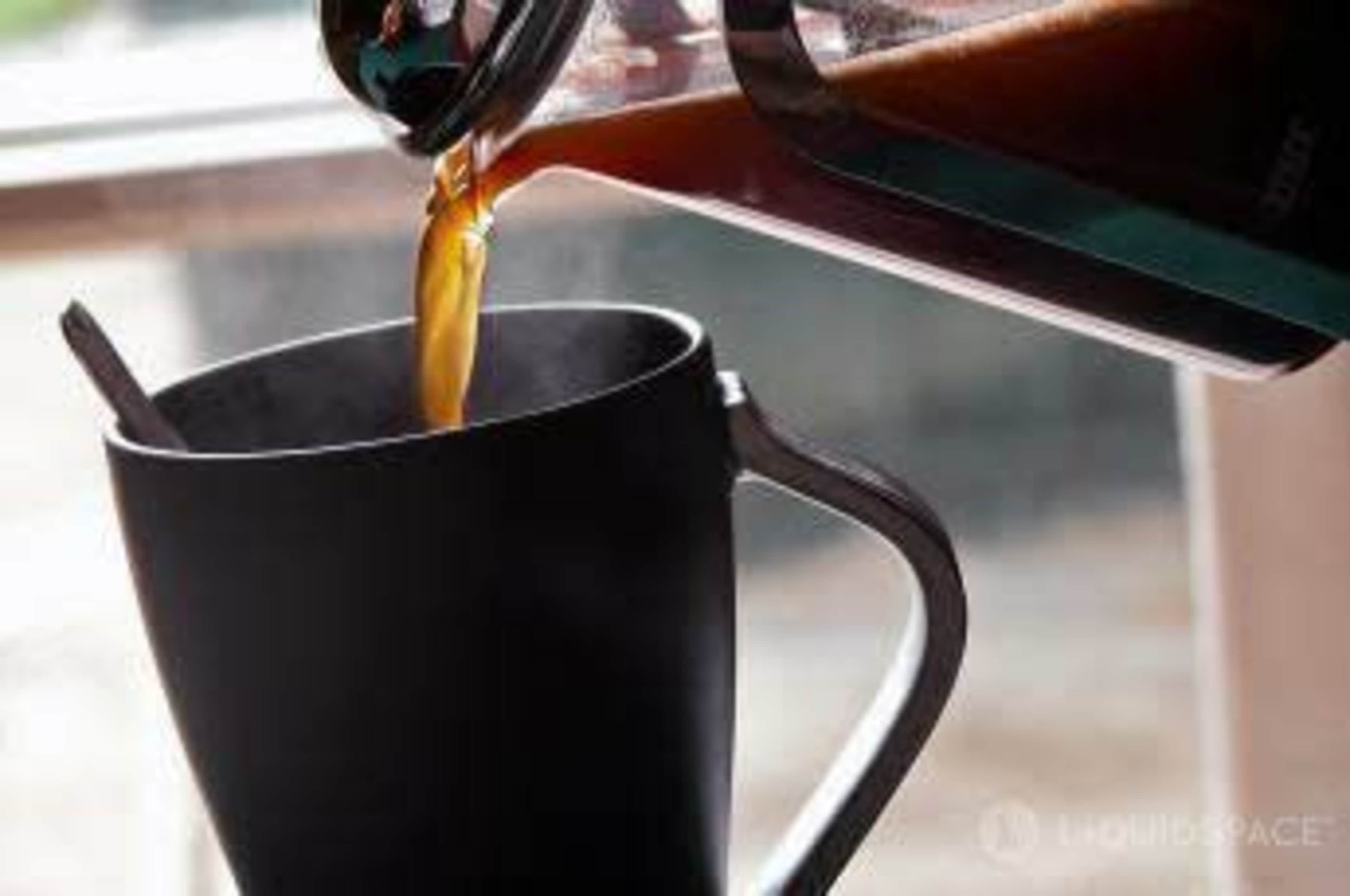 A steaming cup is filled with freshly brewed coffee from a French press.