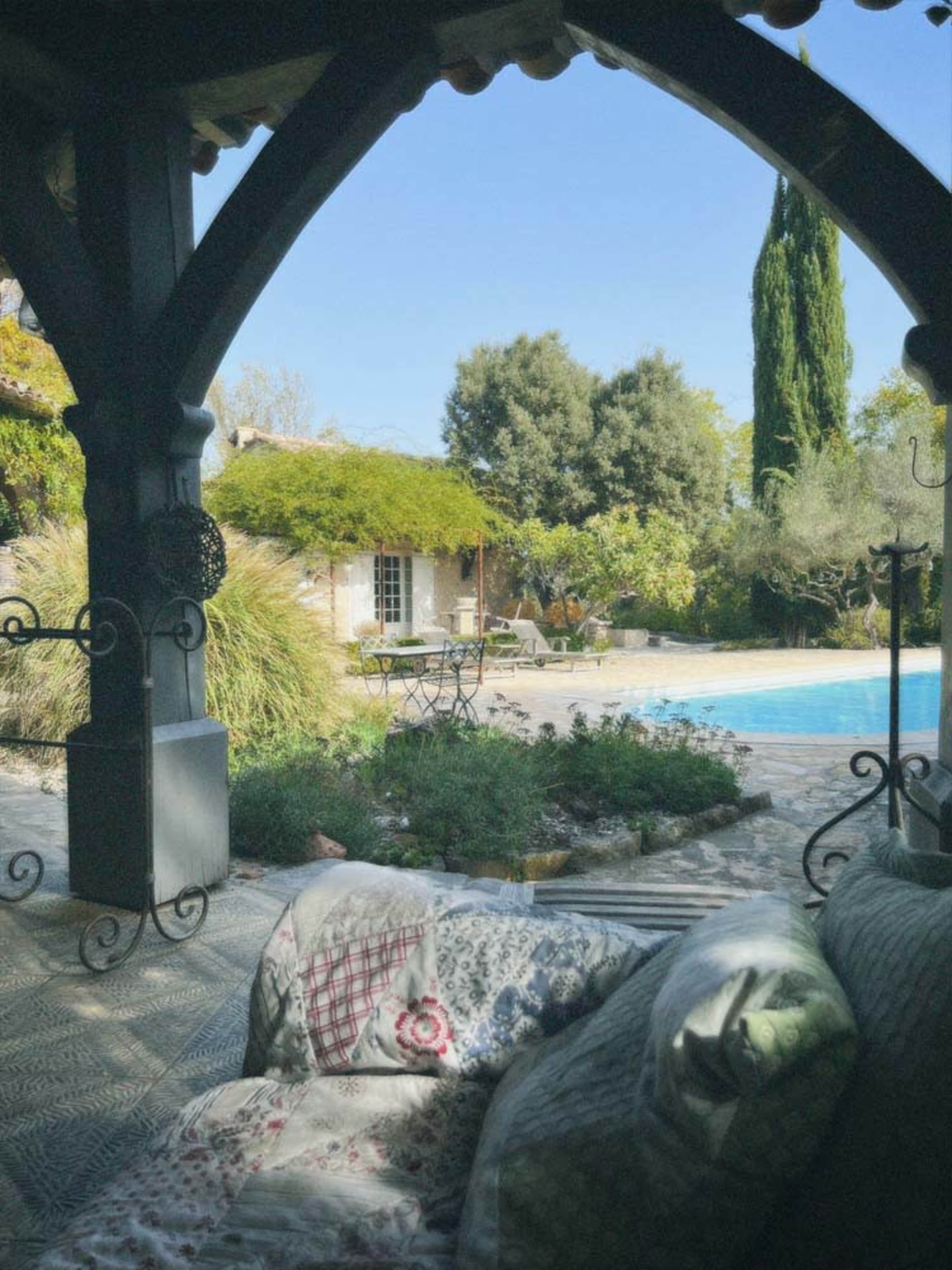 A cozy outdoor seating area with a view of a swimming pool and a house surrounded by trees and greenery.