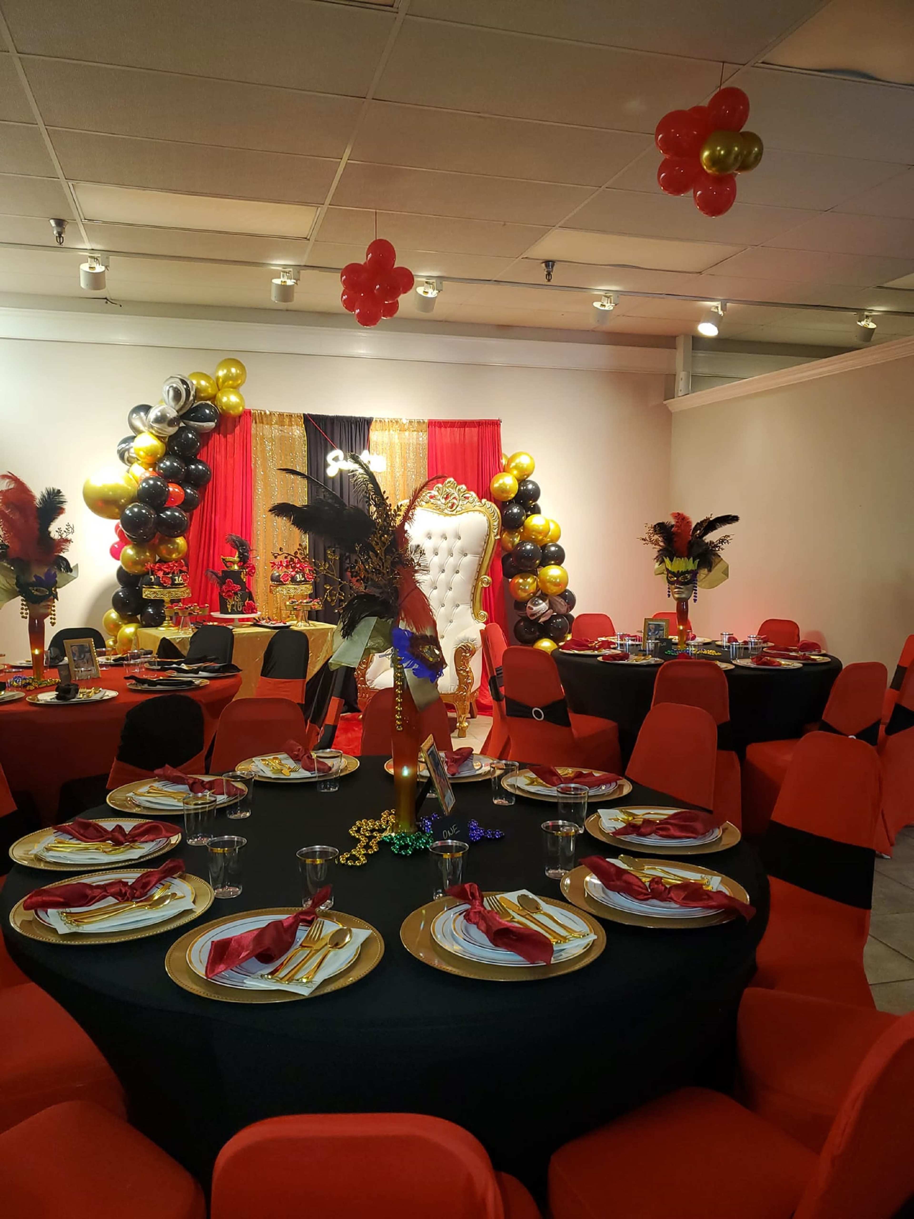 The scene depicts a festive banquet hall set up with circular tables adorned in black tablecloths and red chairs, featuring decorative centerpieces and a backdrop of balloons and a large throne.