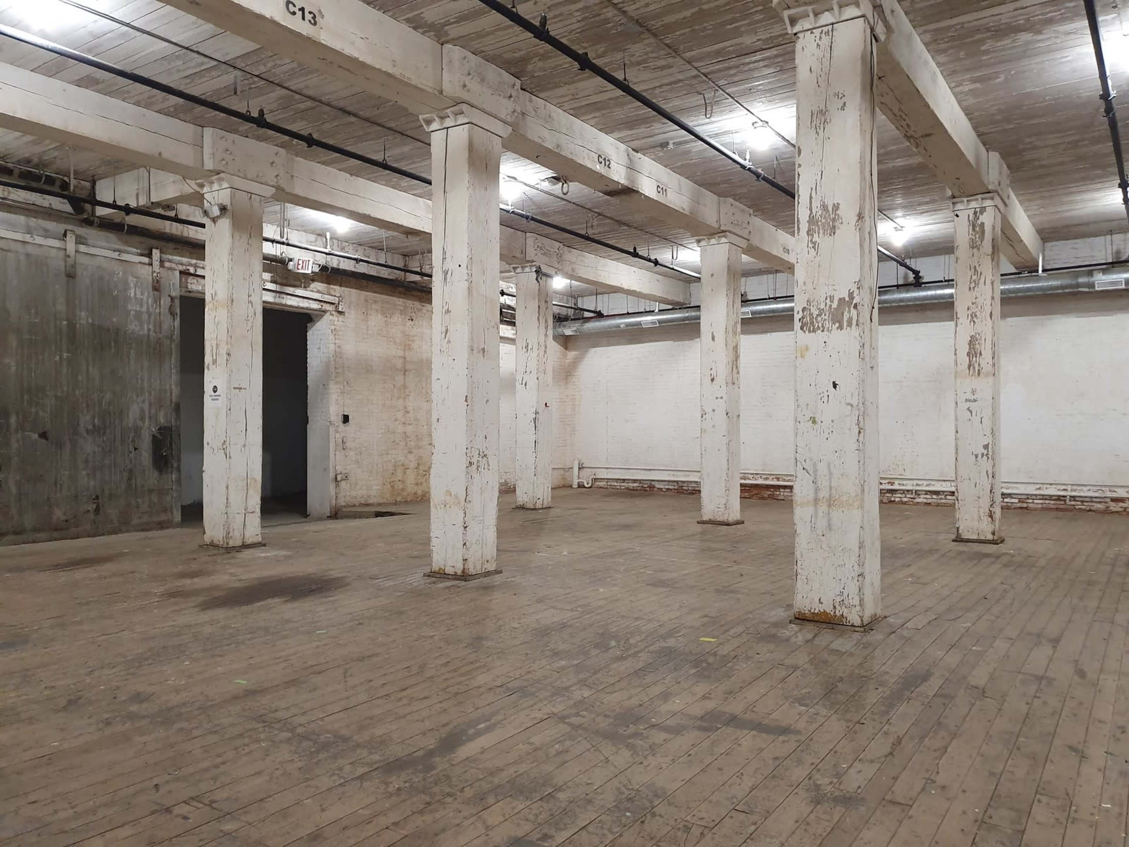 An empty industrial space with wooden floors and several large white columns.