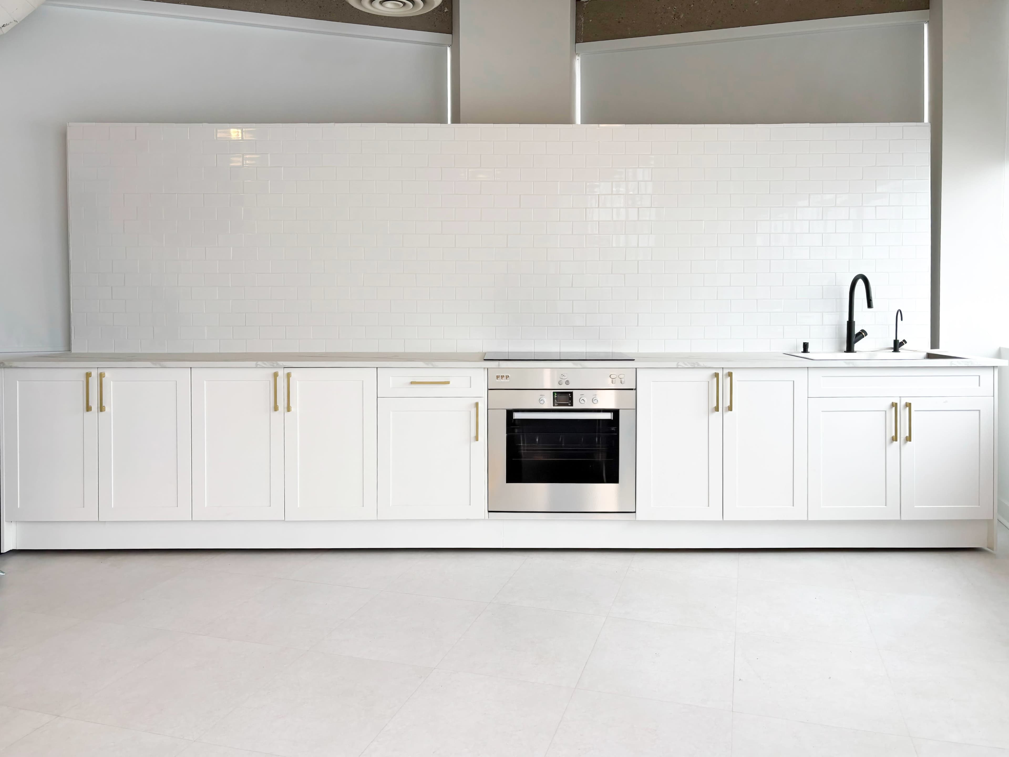 The image shows a modern kitchen with white cabinetry, a built-in oven, and a black faucet against a white tiled backsplash.