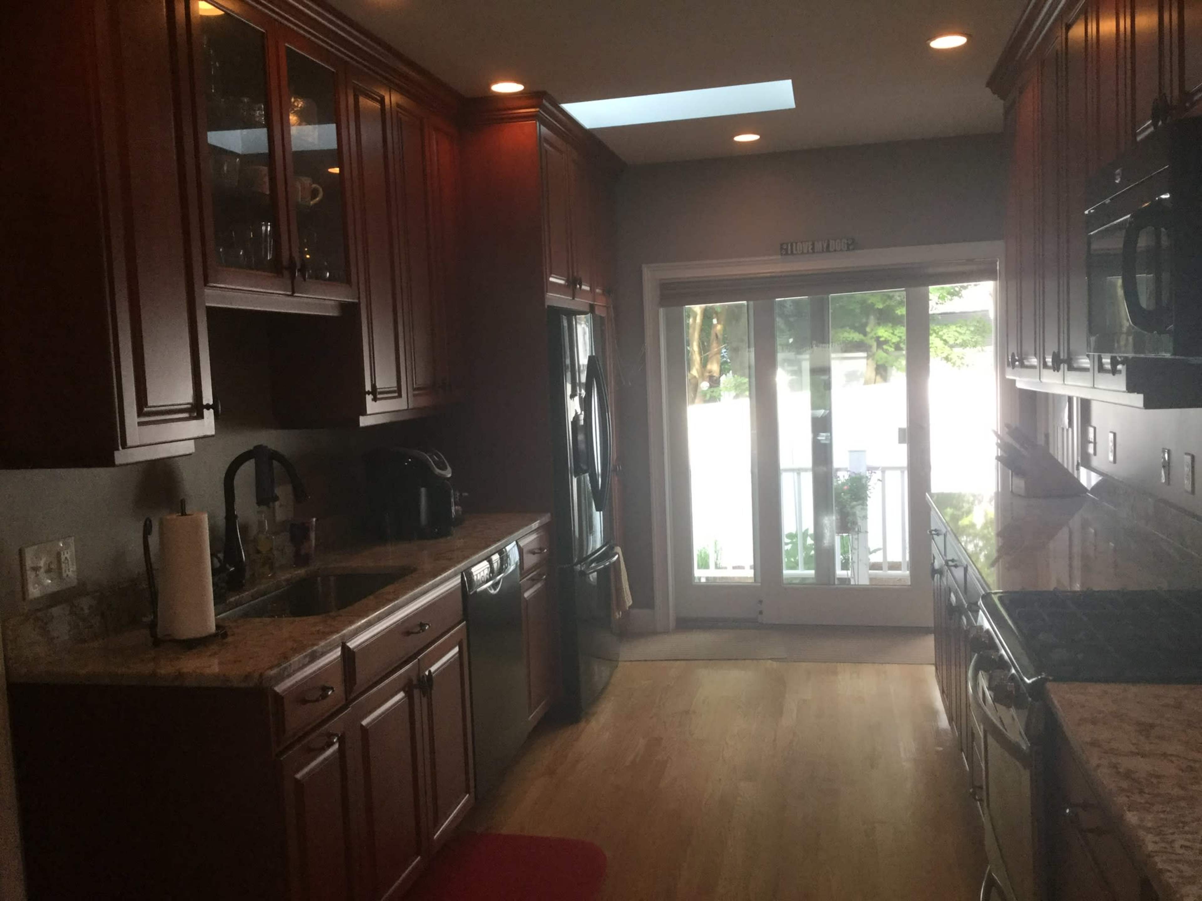 A modern kitchen with wooden cabinets, a stone countertop, and a sliding glass door leading to an outside area.