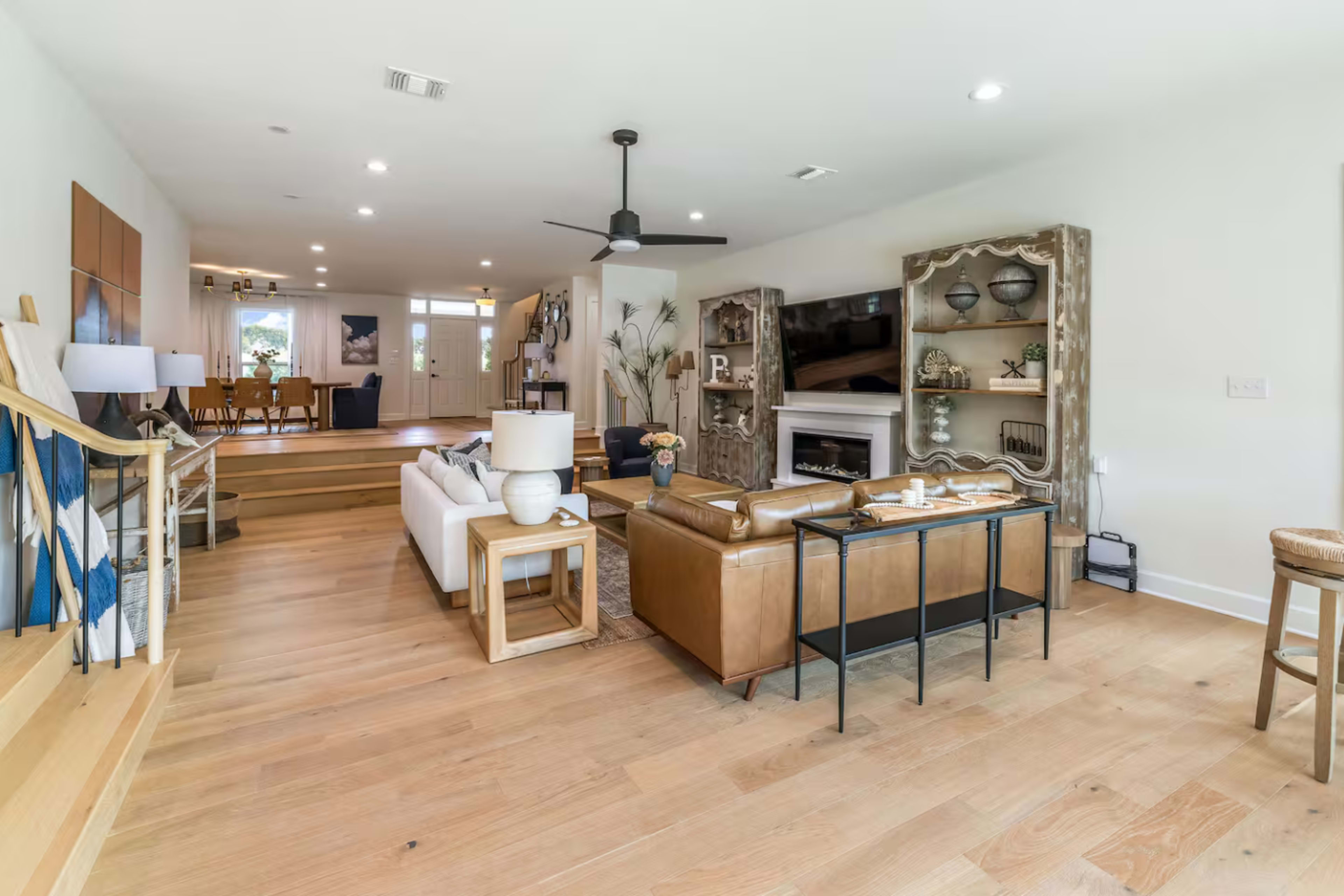 The image shows a modern living room featuring a combination of a leather couch, a white sofa, and a large entertainment unit, with a dining area visible in the background.