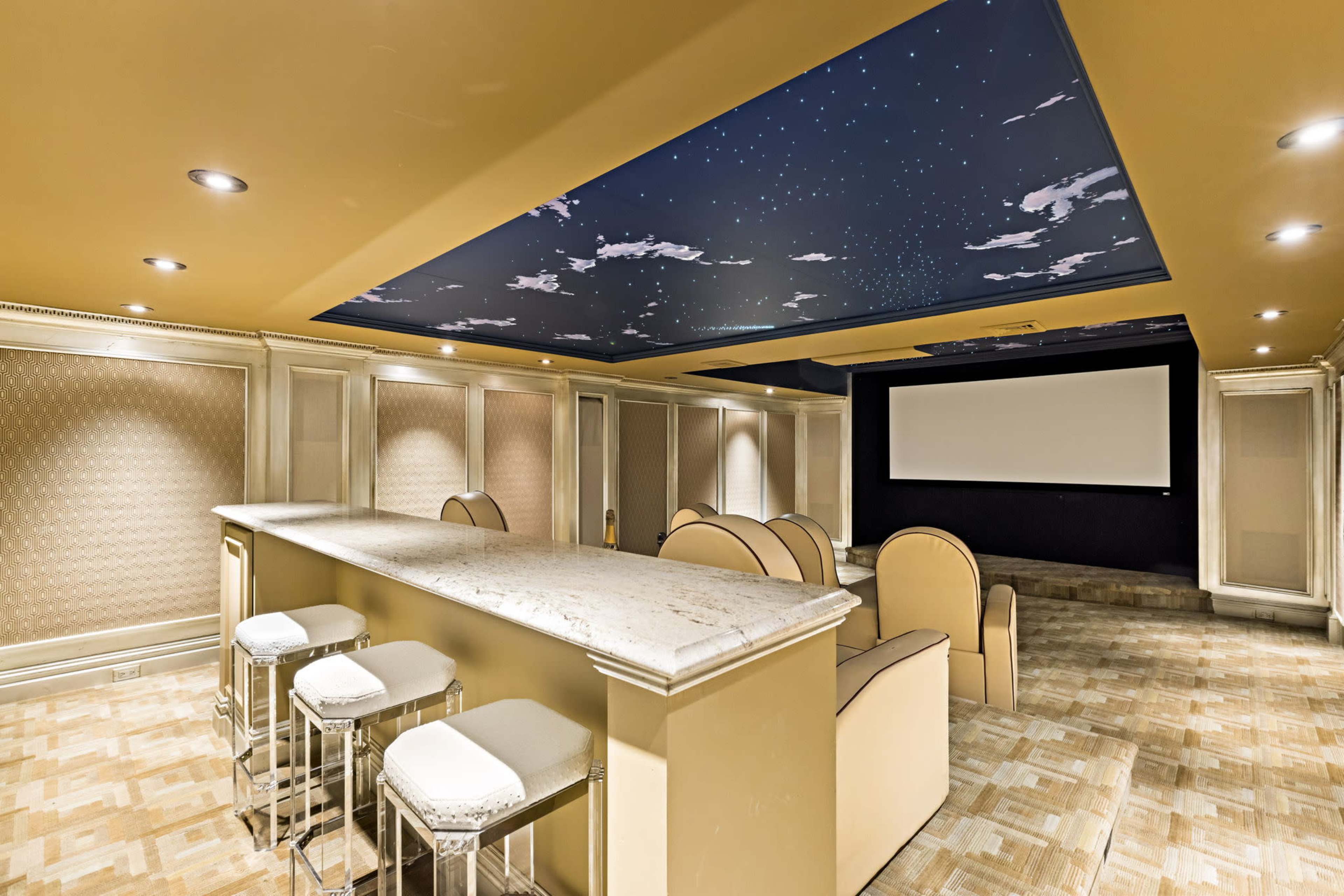 The image shows a modern home theater with a marble bar, plush seating, and a starry ceiling, featuring a large screen for viewing.