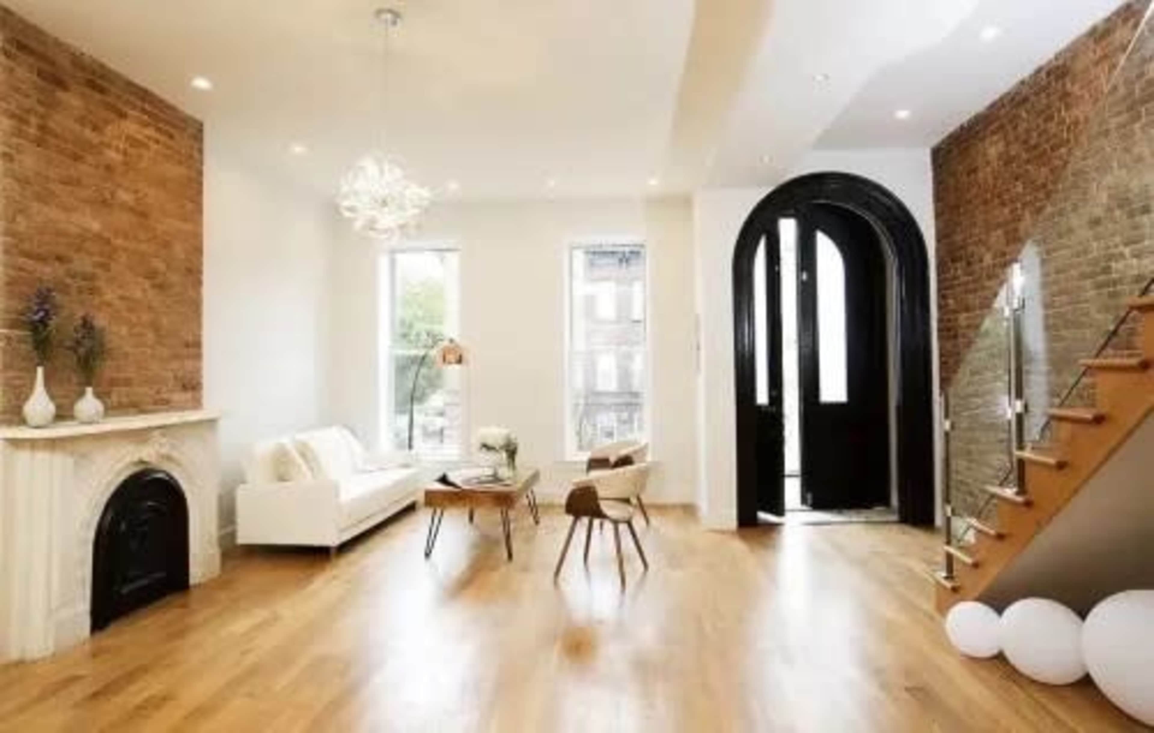 The image shows a modern living space with a brick accent wall, hardwood flooring, a white sofa, and a staircase leading to an upper level.