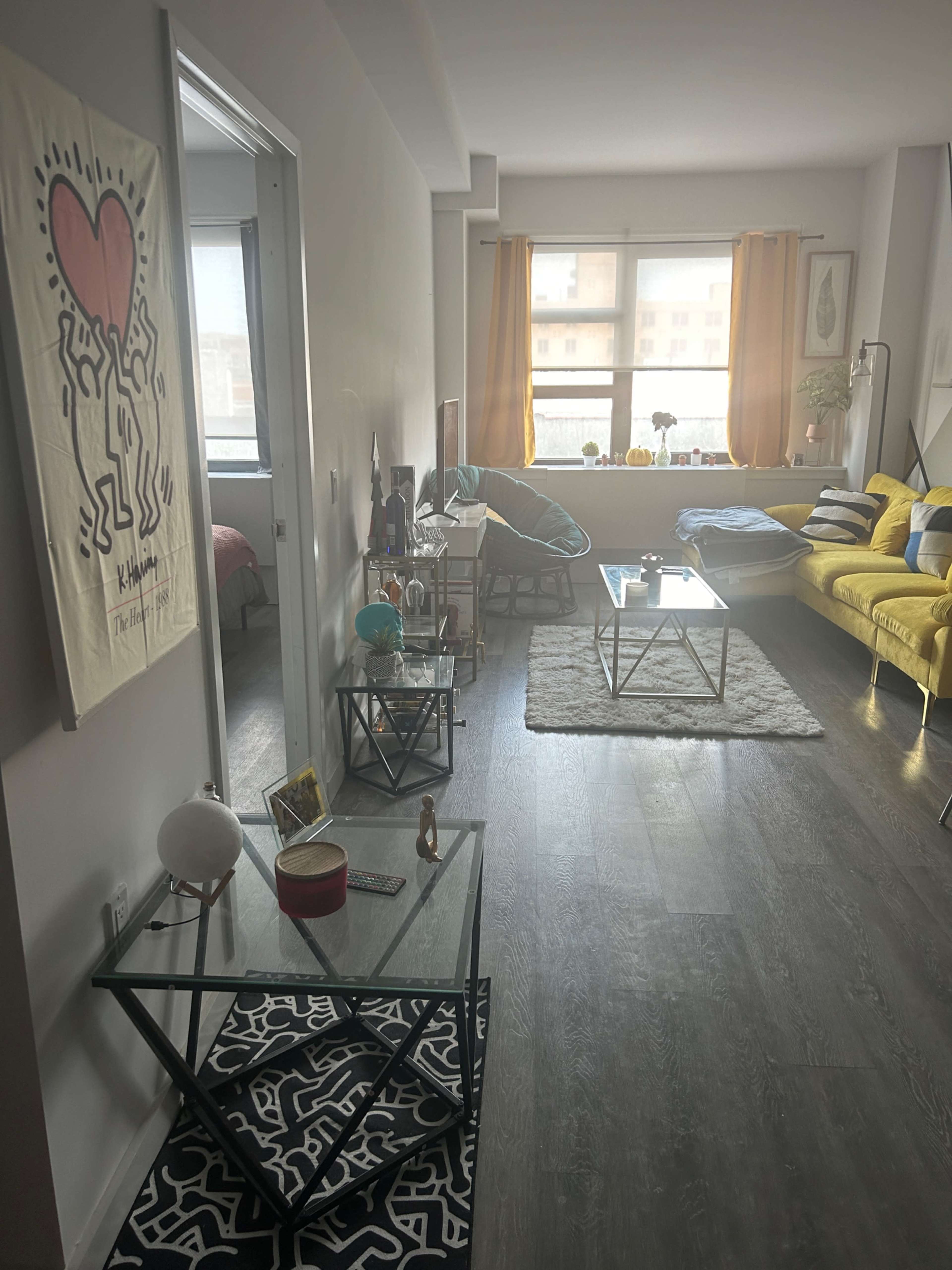 The image shows a modern living room with a yellow couch, a glass coffee table, and decorative elements throughout the space.