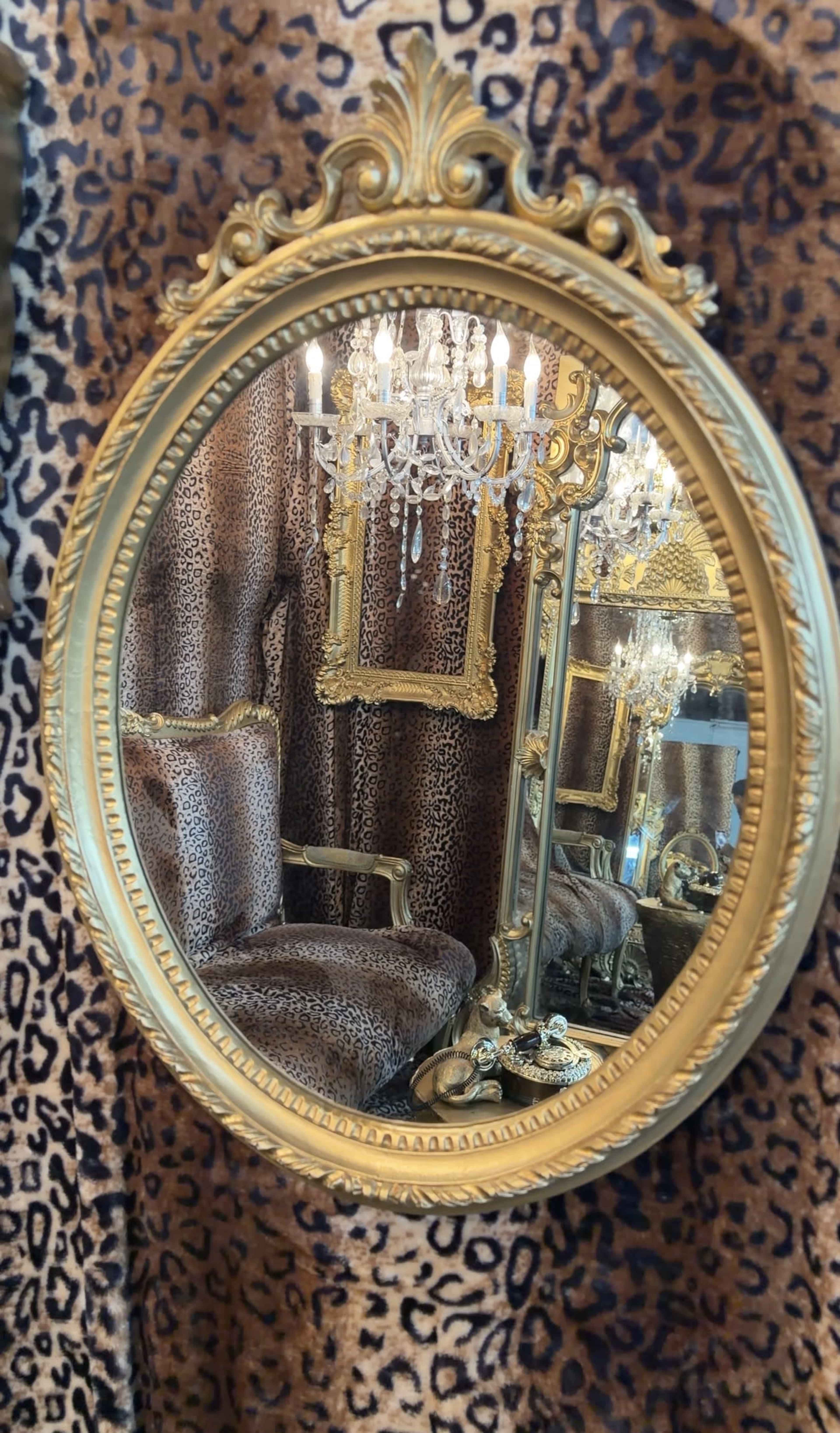 A gilded mirror reflects a luxurious leopard-print interior featuring a chandelier and an ornate frame.