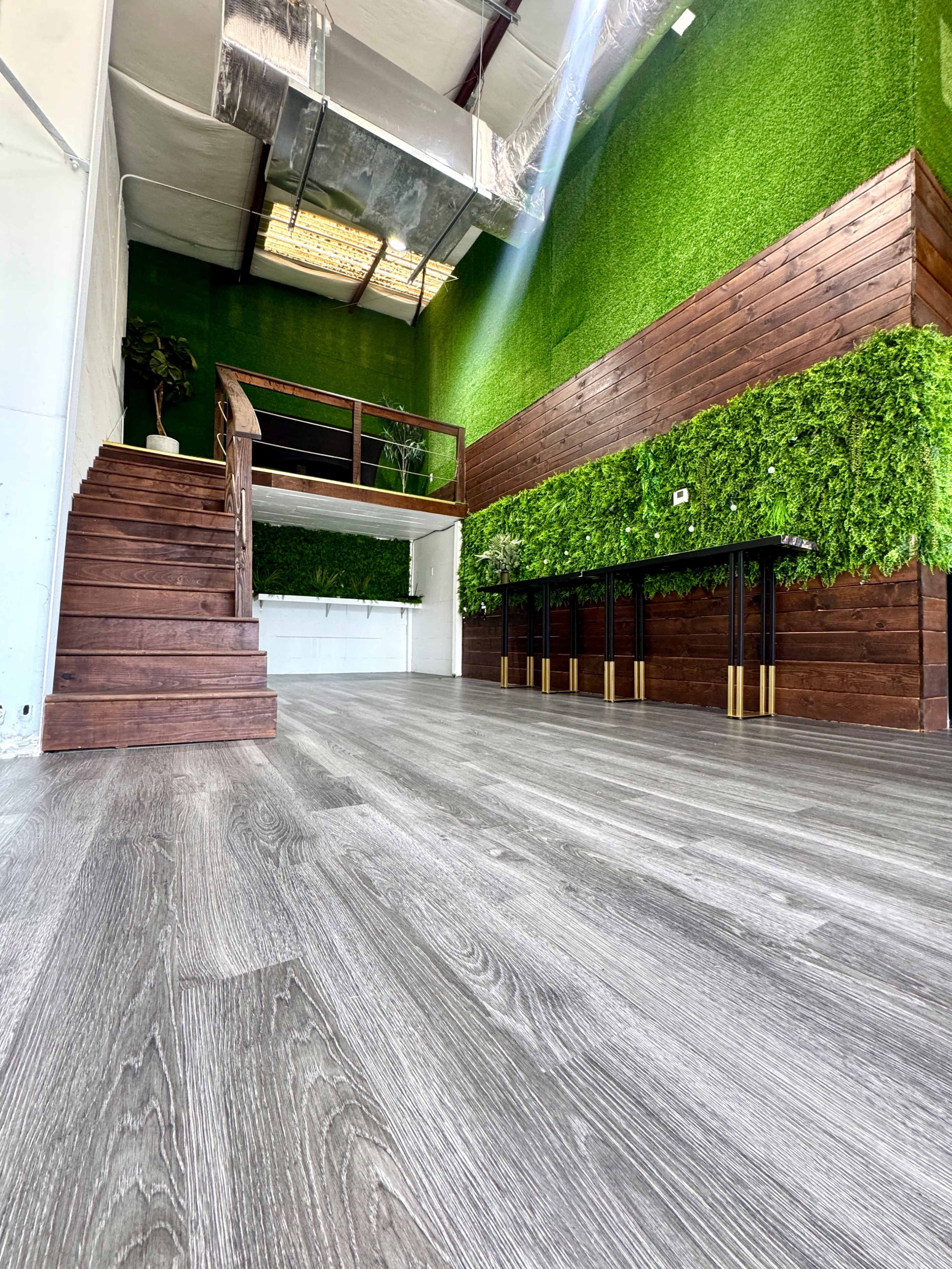 The image shows a spacious interior with a staircase, wooden accents, and a wall covered in greenery, all illuminated by natural light.