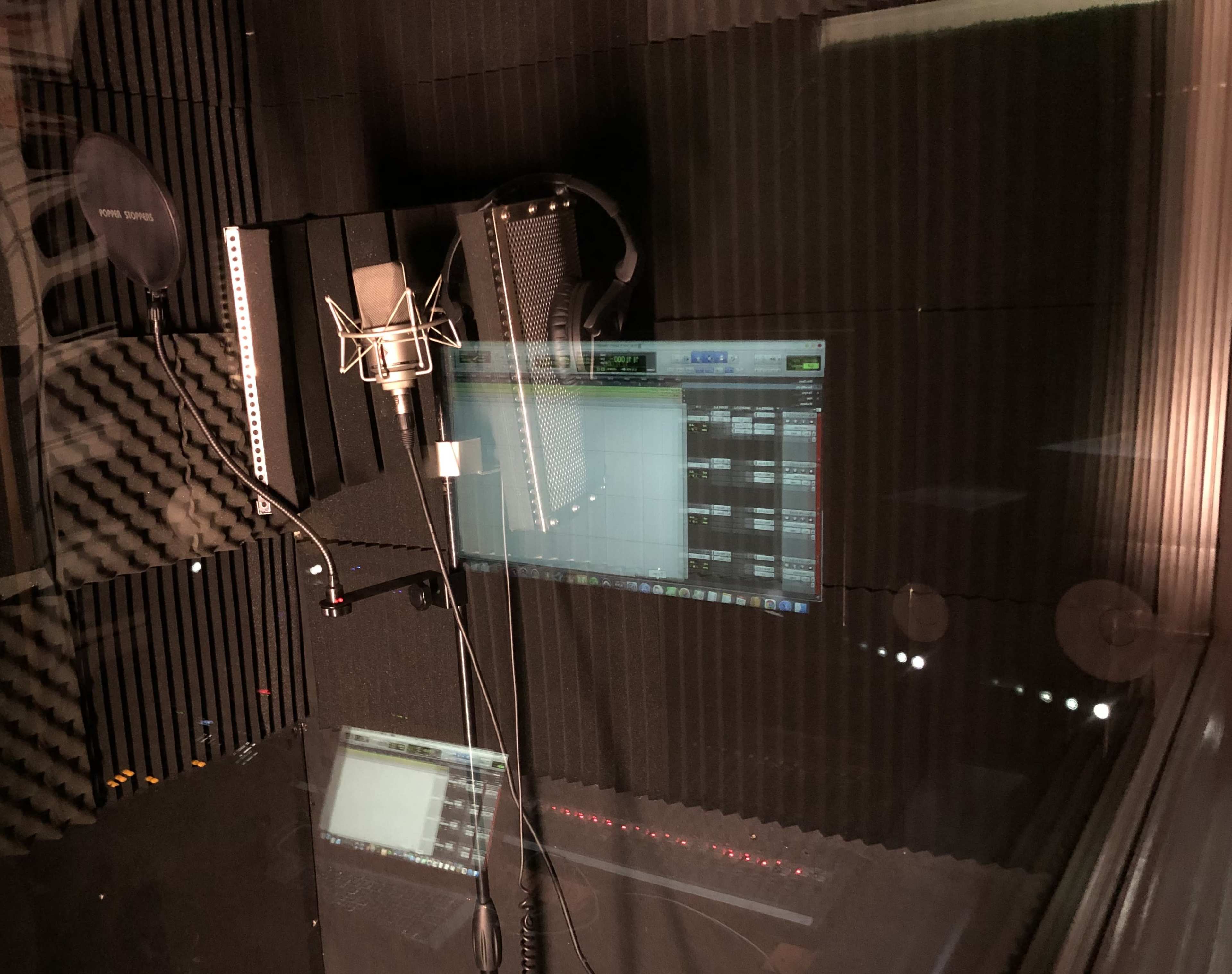 A recording studio with a microphone, soundproof walls, and a computer screen displaying audio software.