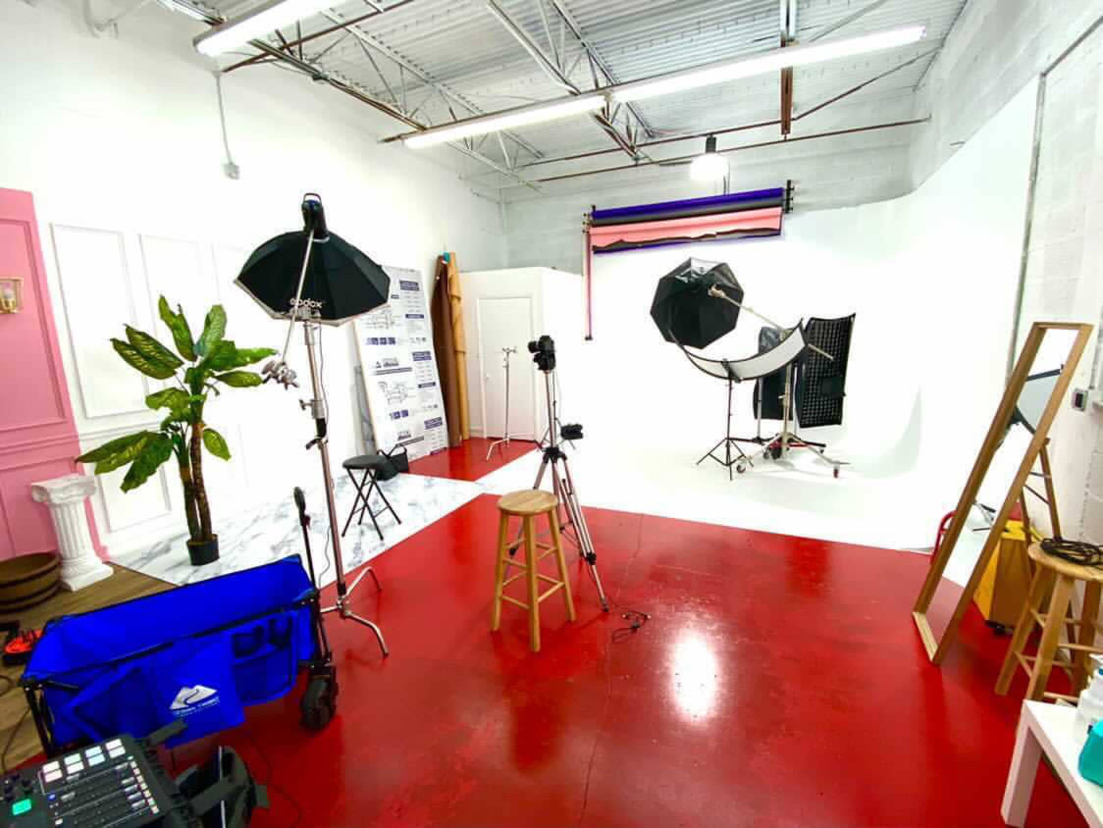 A photography studio with red flooring, various lighting equipment, a backdrop, and a few props arranged throughout the space.