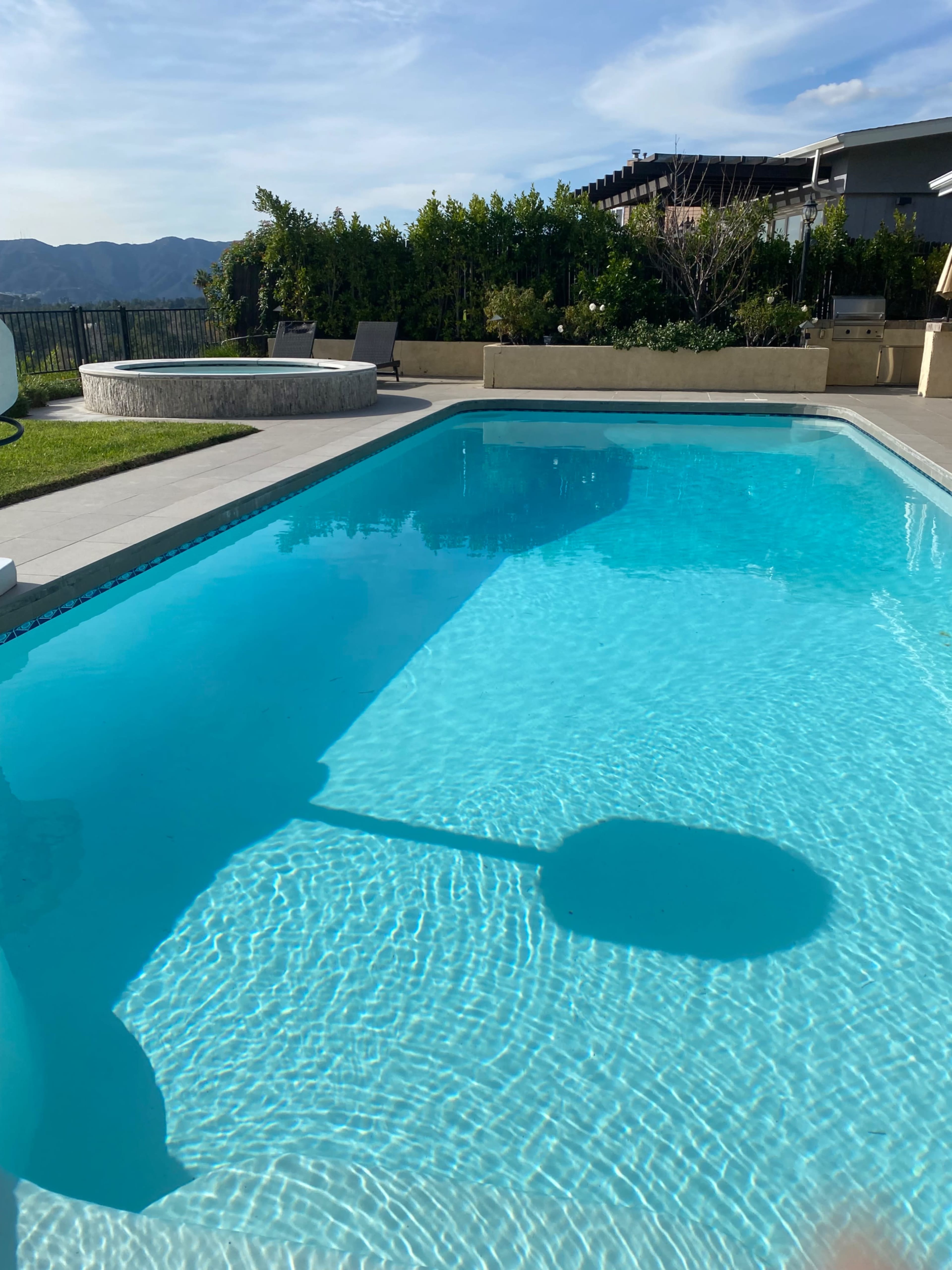 A clear swimming pool reflects the surrounding landscape and structures under a sunny sky.