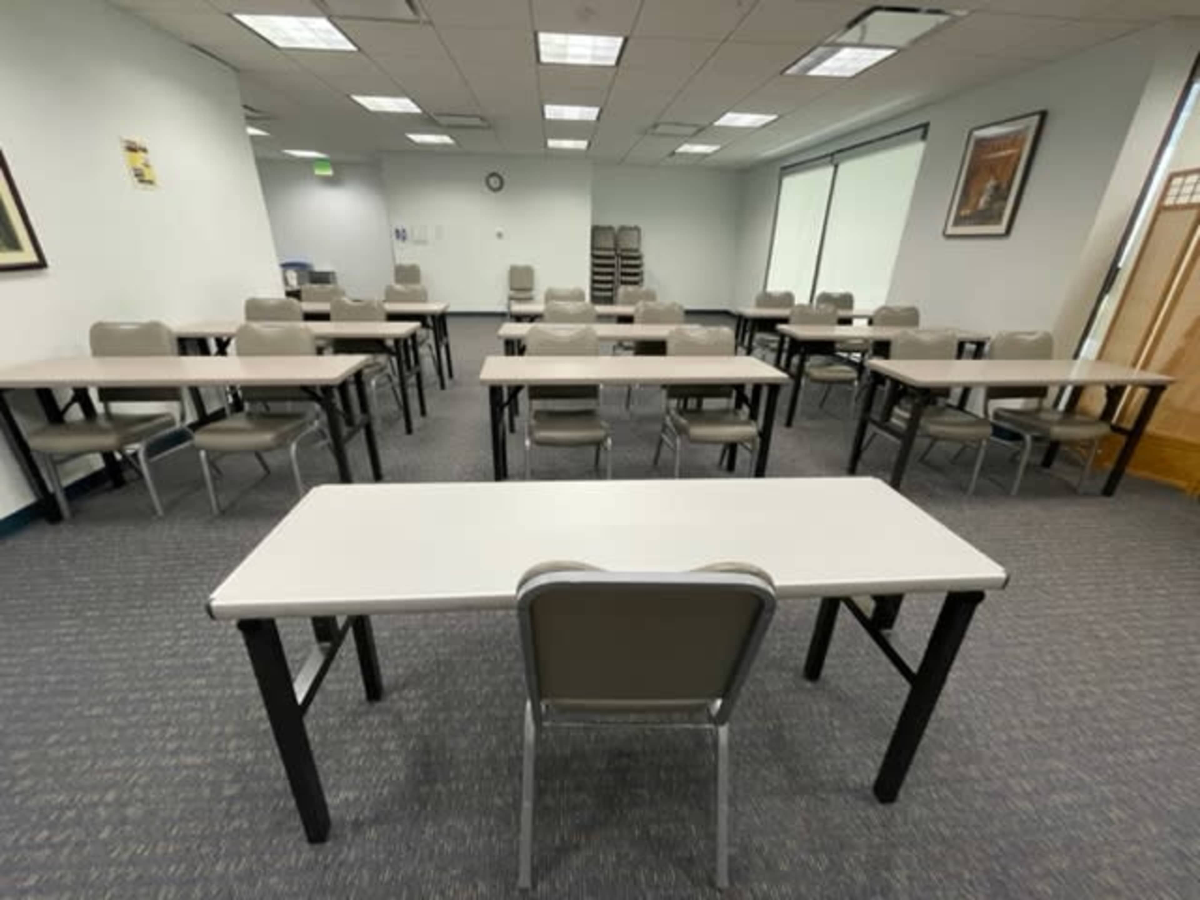 The image shows a classroom setup with several tables arranged in a grid pattern, facing a central area with a single chair positioned at the front table.